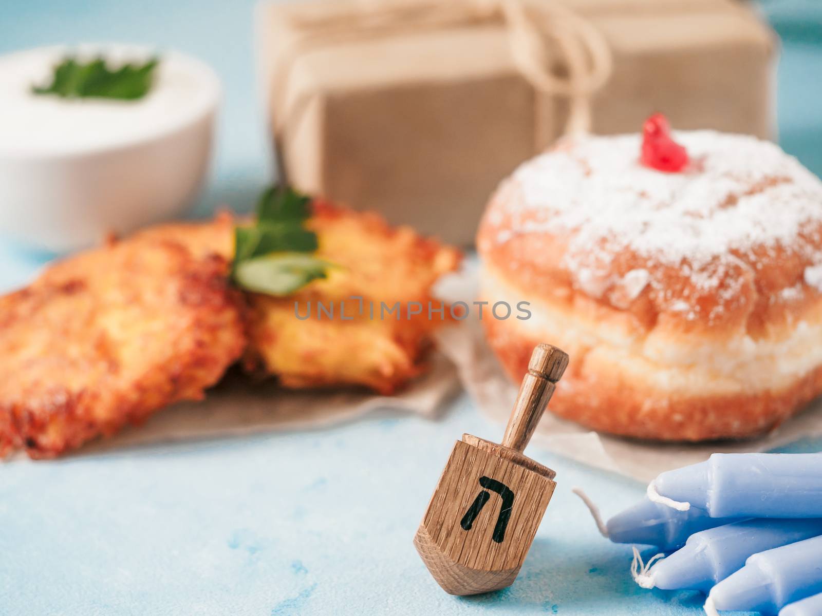 Jewish holiday Hanukkah concept and background. Hanukkah food doughnuts and potatoes pancakes latkes, giftbox, candle and traditional spinnig dreidl on blue background. Copy space for text.