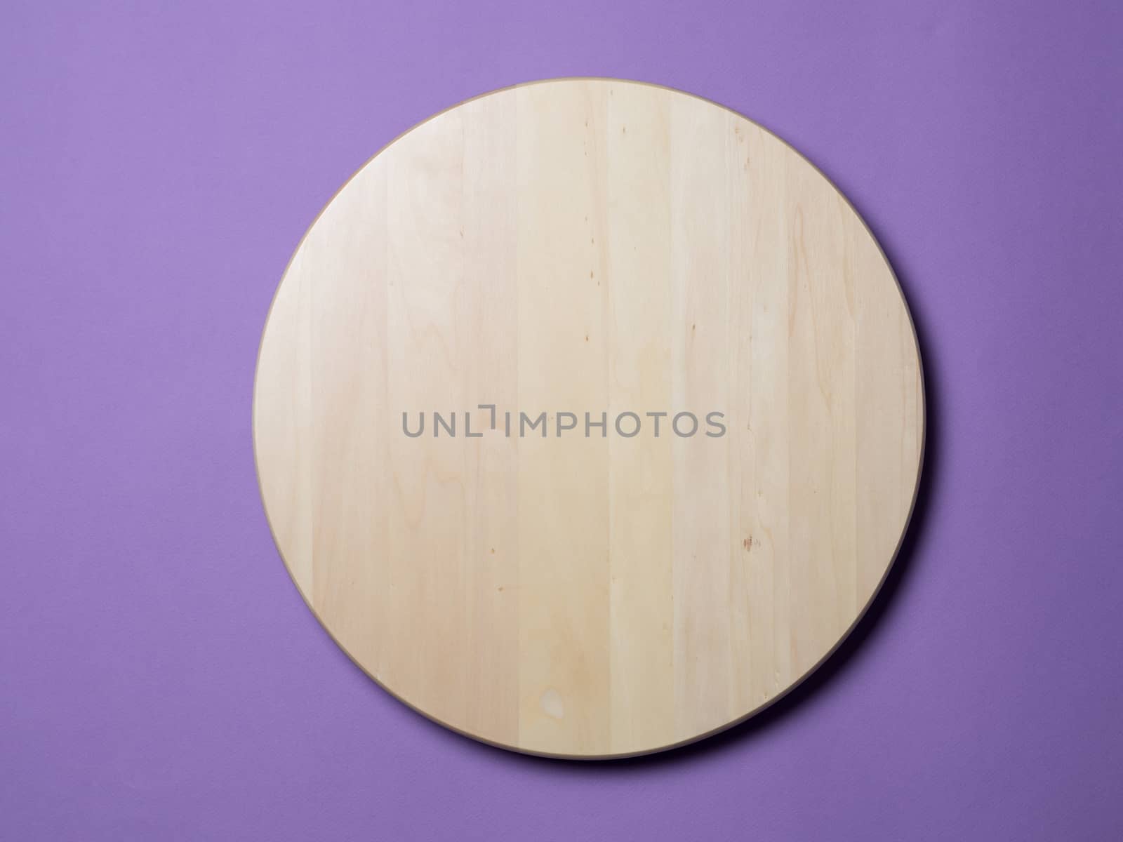 Empty wooden round tray or trencher, cutting board on lilac background. Hard light. Top view or flat lay.