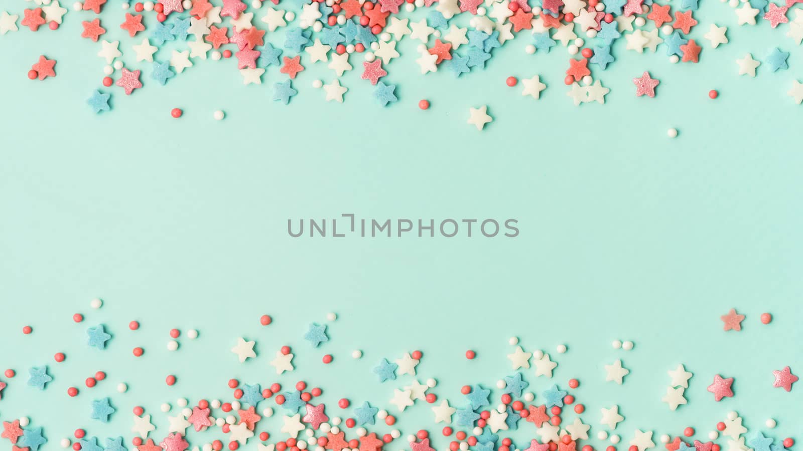 Festive border frame of colorful pastel sprinkles on blue background with copy space in center. Sugar sprinkle dots and stars, decoration for cake and bakery. Top view or flat lay. Banner