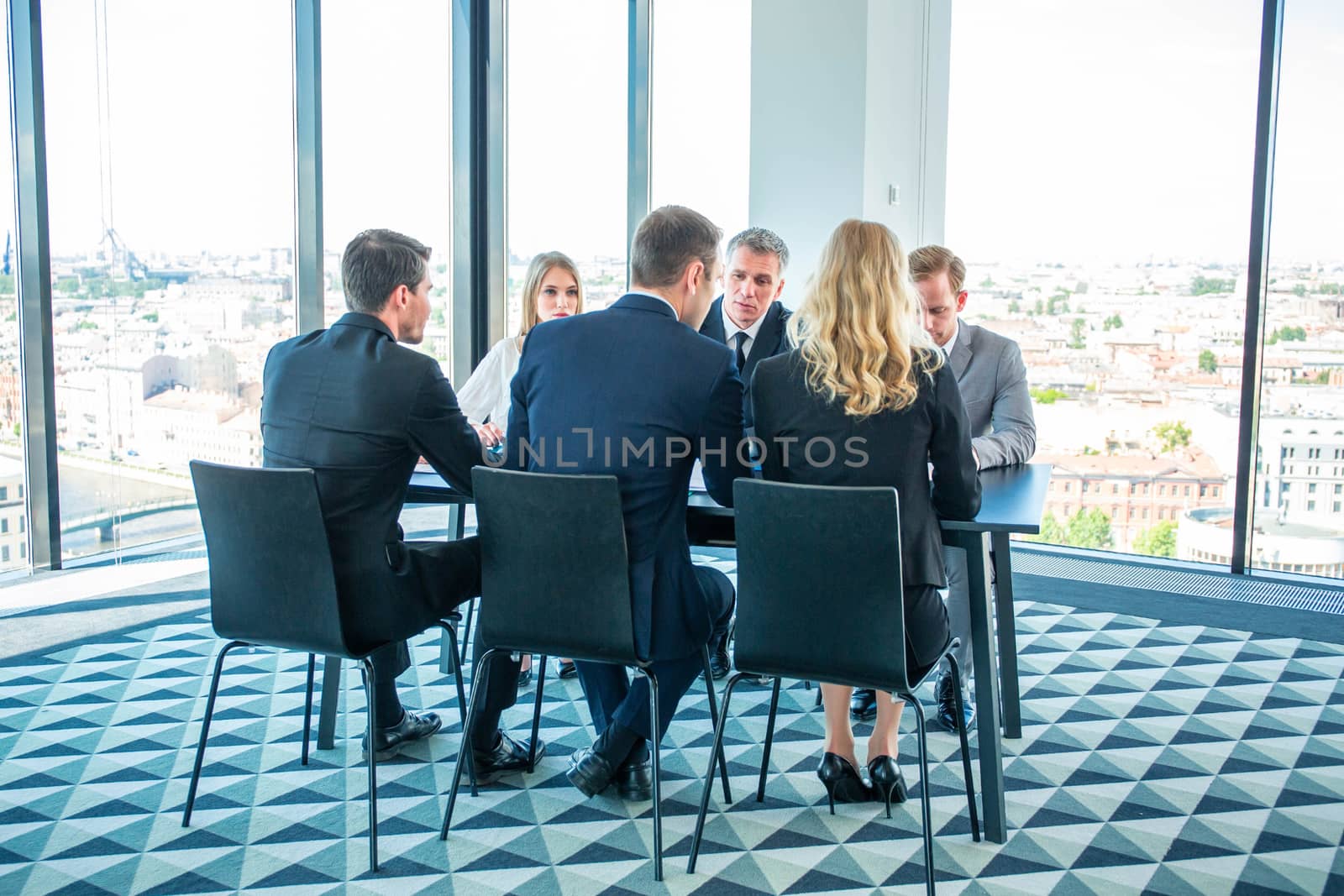 Executives participating in meeting taking seat at office table. Panoramic window with view on city on background