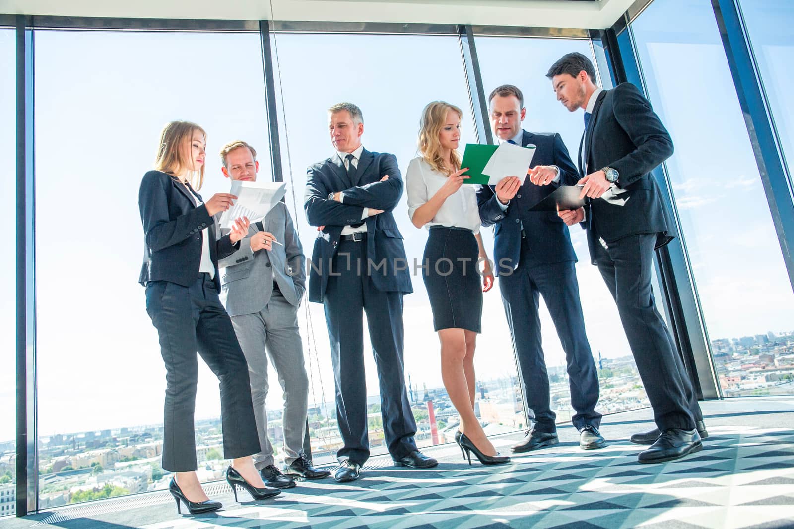 Business men and women standing together in a panoramic office and talking discussing financial reports
