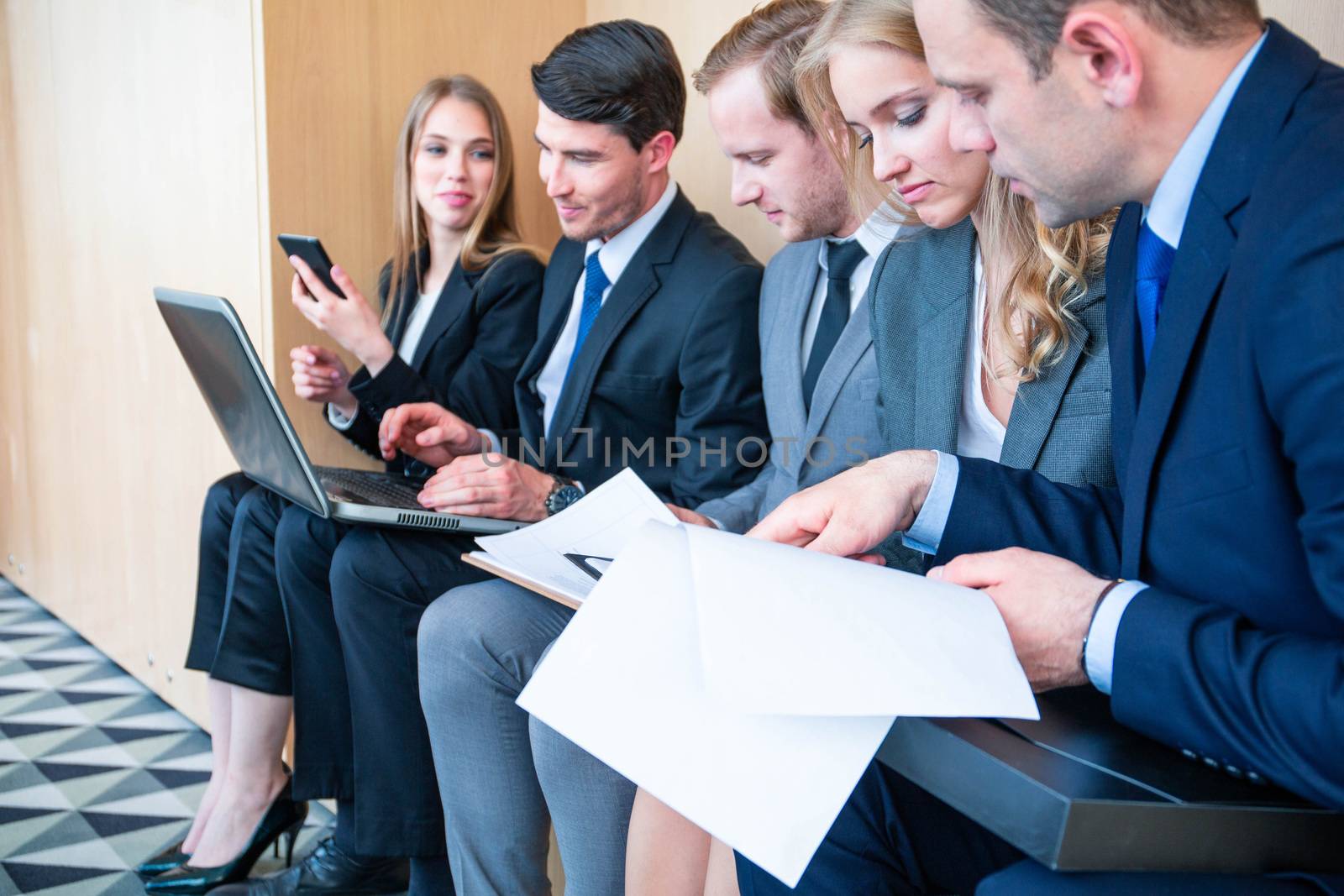Group of business people is sitting in a row in an office lobby and waiting for the job interview or working with documents and laptops