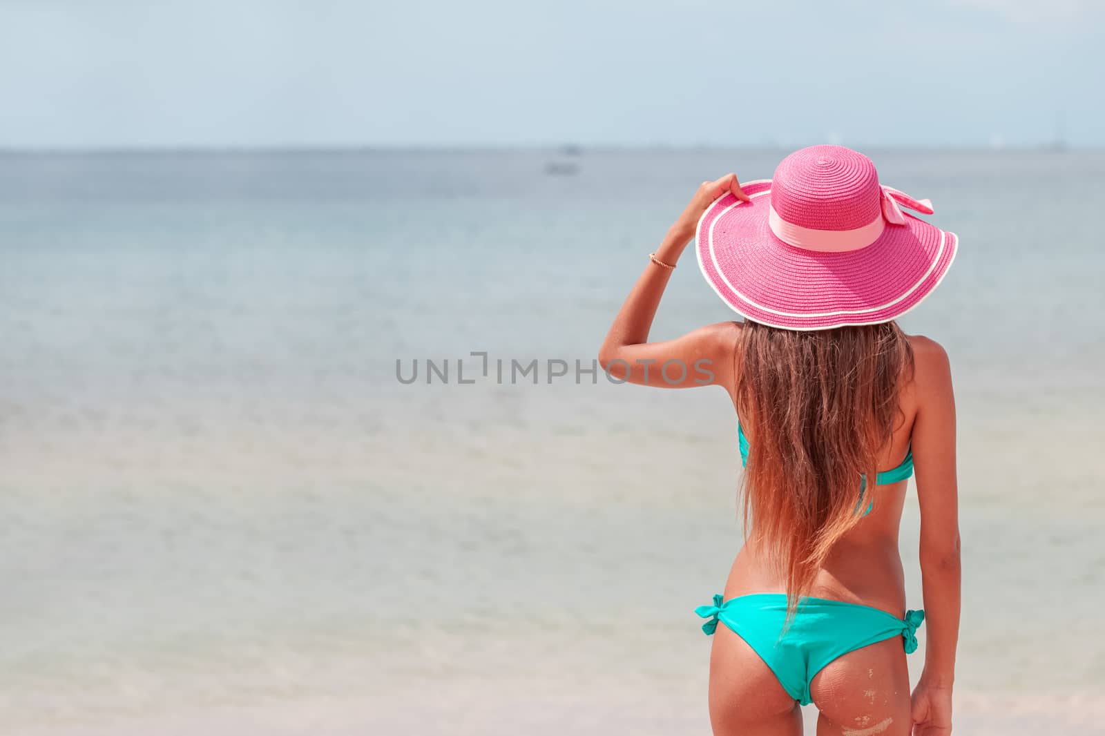 Beach vacation concept. Hot beautiful woman in sunhat and bikini standing enjoying looking view of beach ocean on hot summer day.
