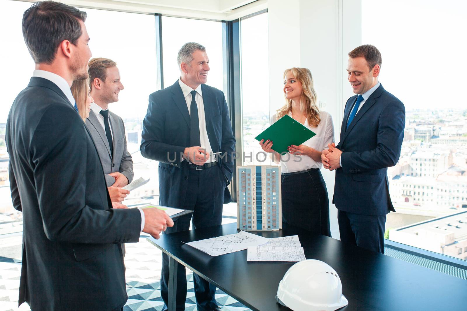 Meeting of architects and business investors, model of modern multi storey residential building house plans and hardhat on table , construction planning concept