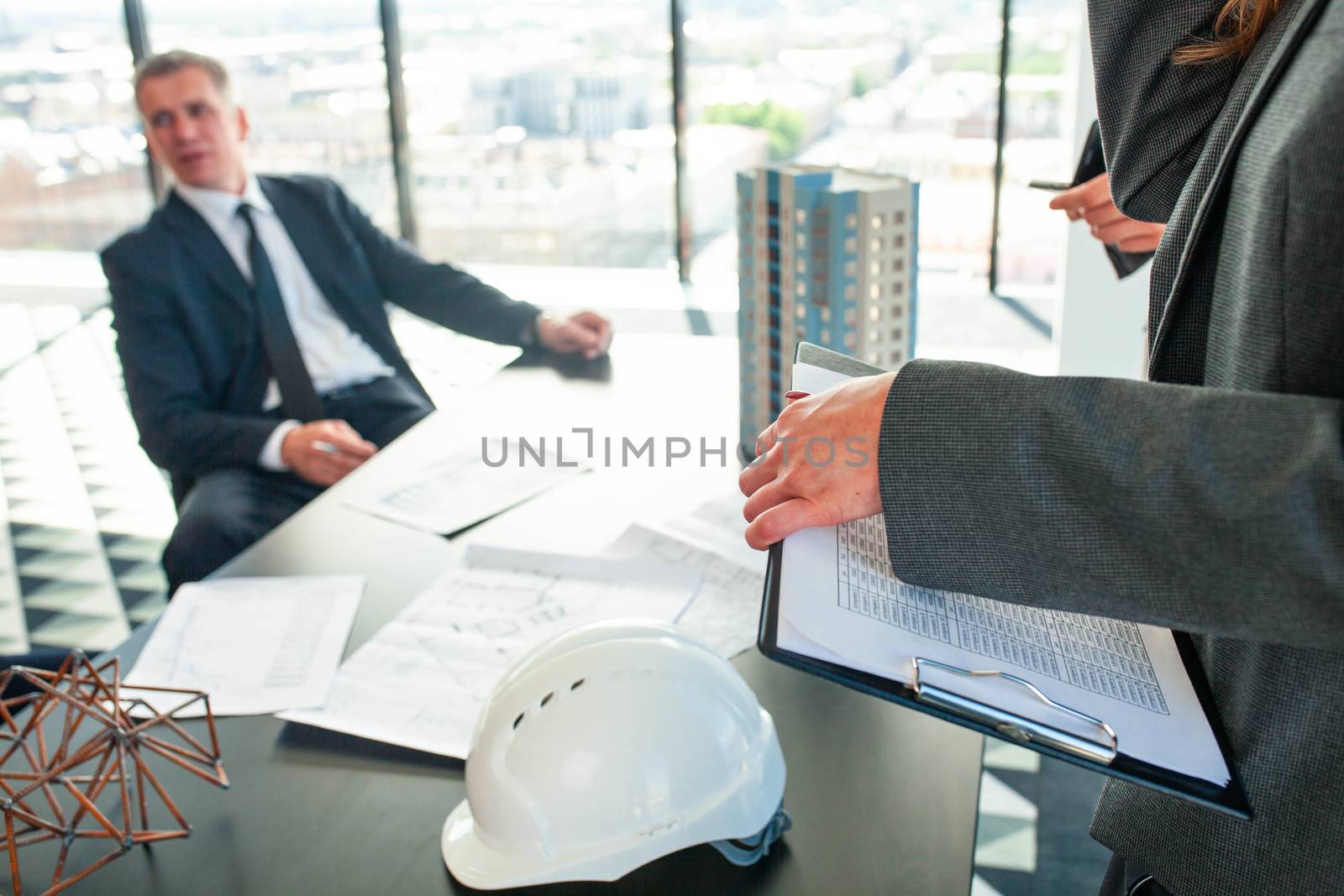 Meeting of architects and business investors, model of modern multi storey residential building house plans and hardhat on table , construction planning concept