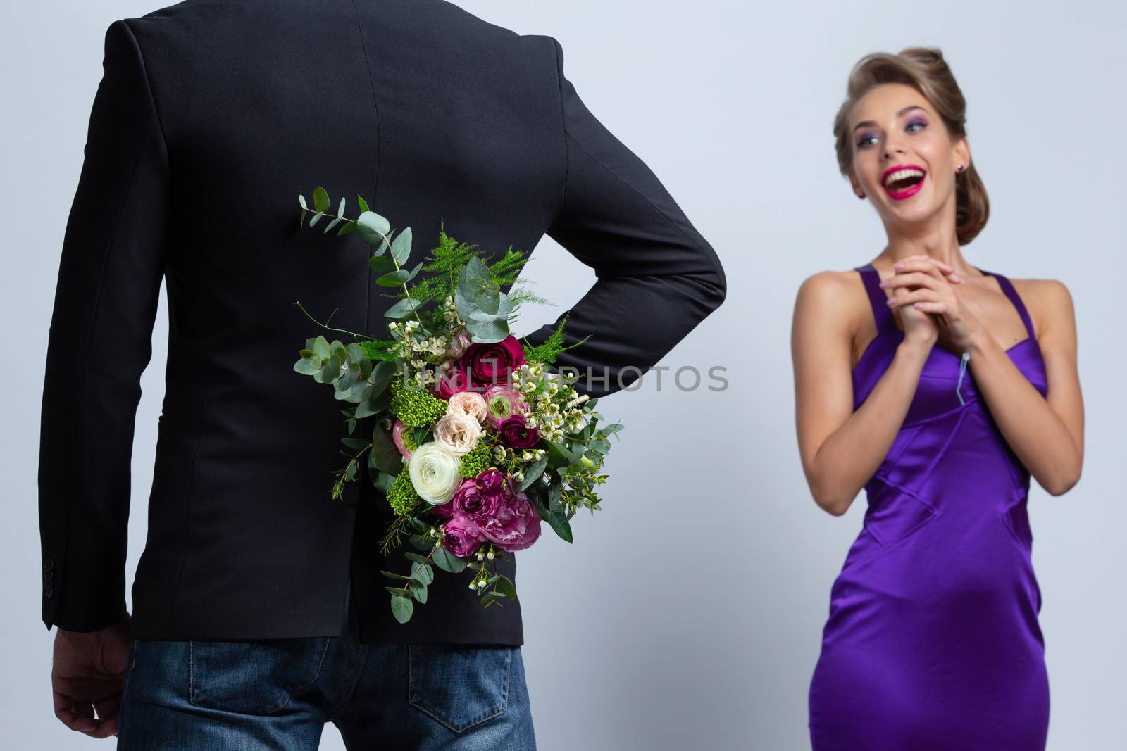 Man hiding bouquet of flowers behind his back comind to date with surprised woman