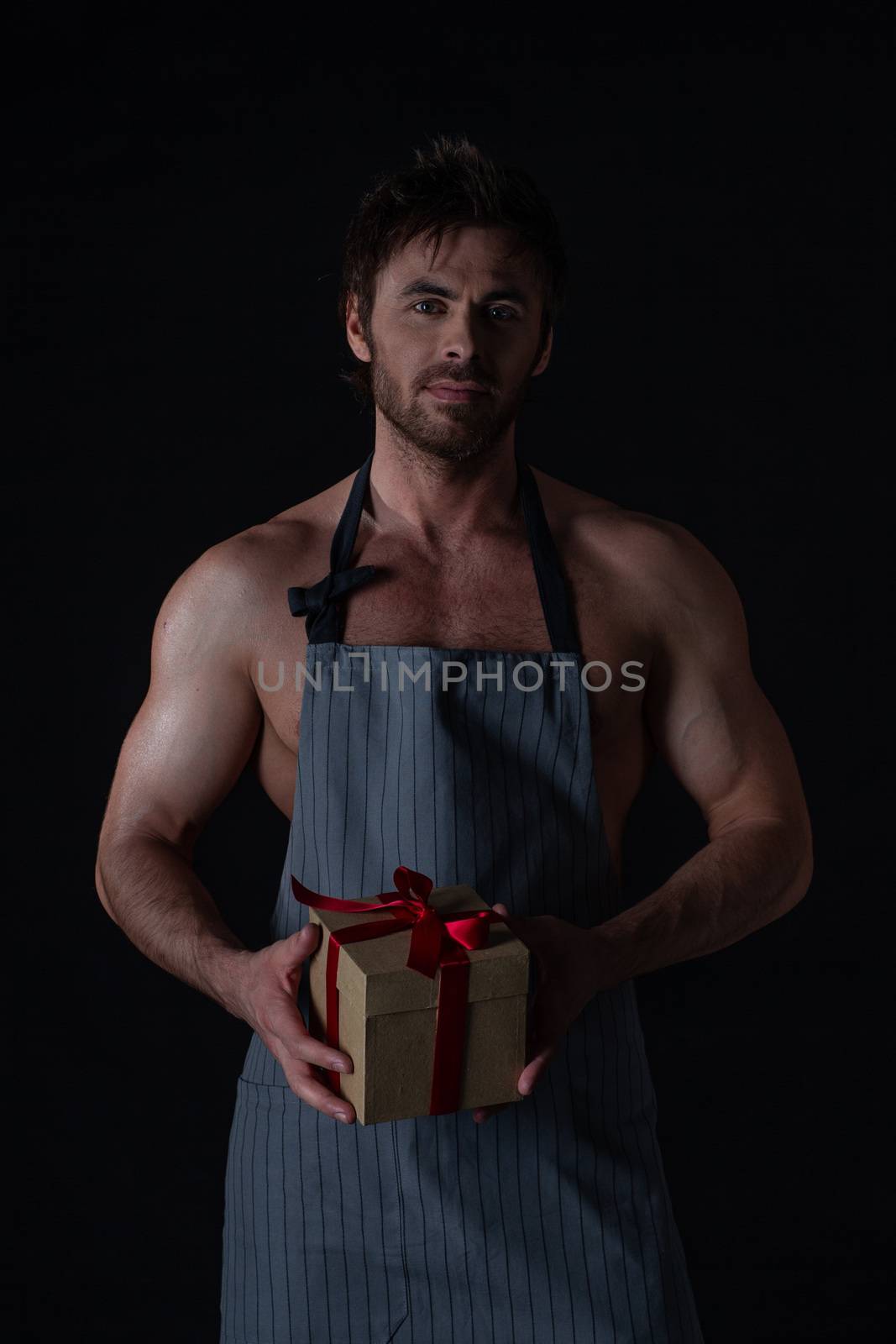 Fun image of naked man only in apron holding Valentines or anniversary day gift on black background