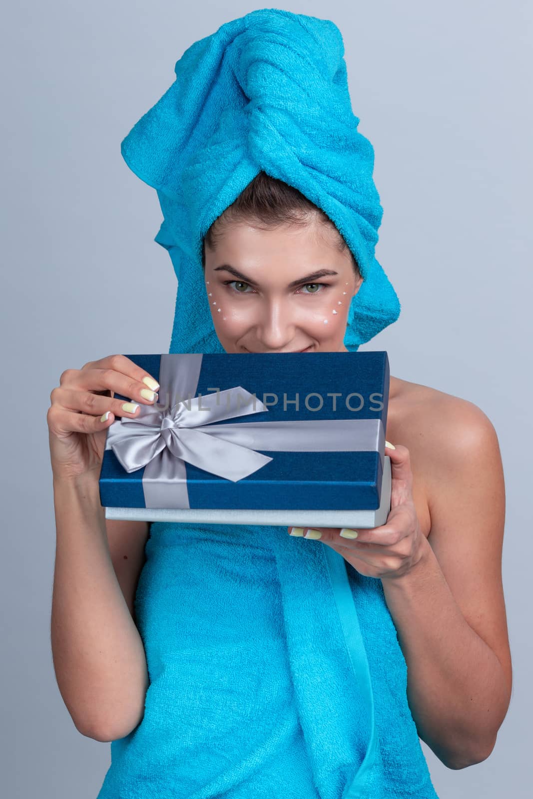 Beautiful woman with towel on head applying creme after shower and open gift box