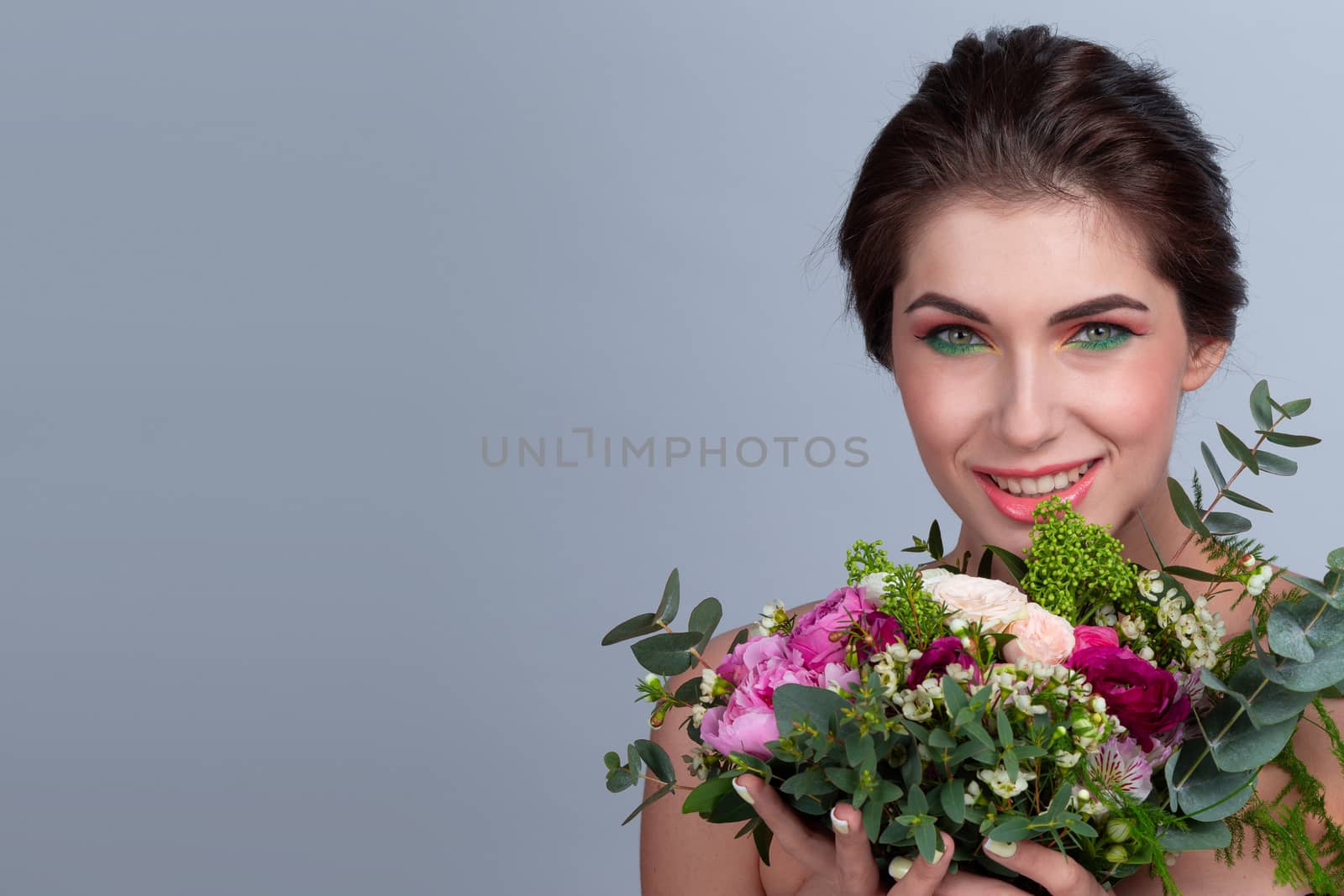 Beautiful woman with stylish make-up holding bouquet of flowers on gray background