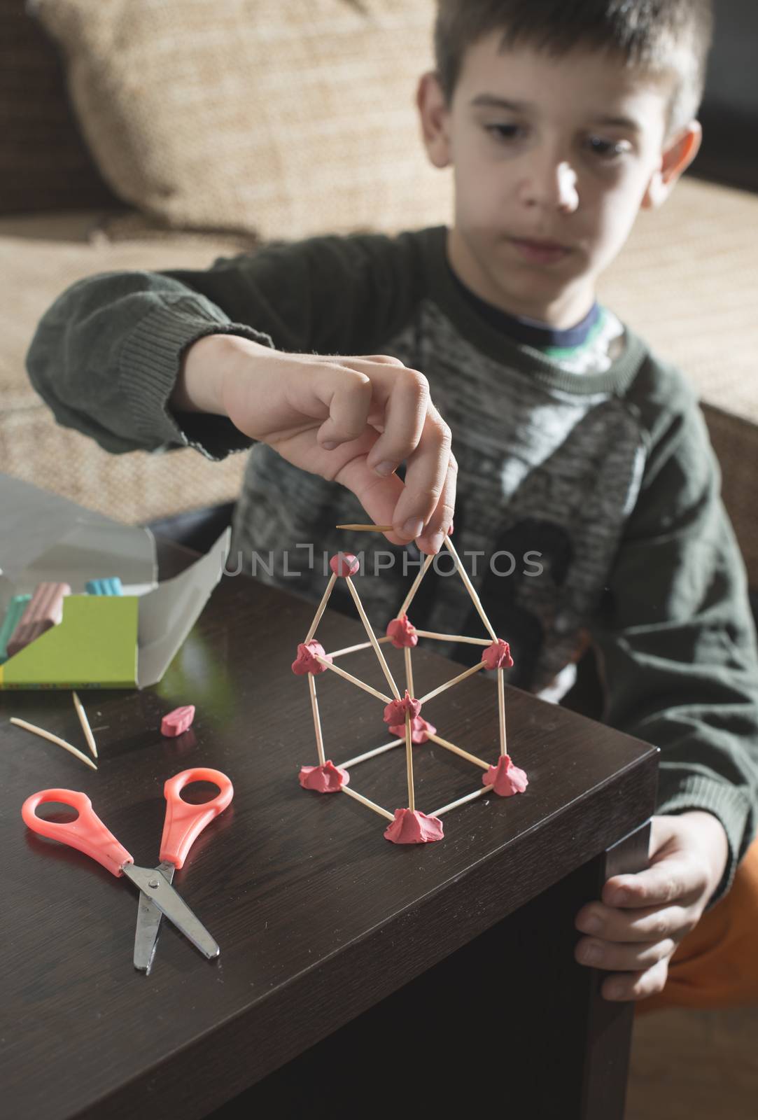 Child make house with wooden sticks and plasticine