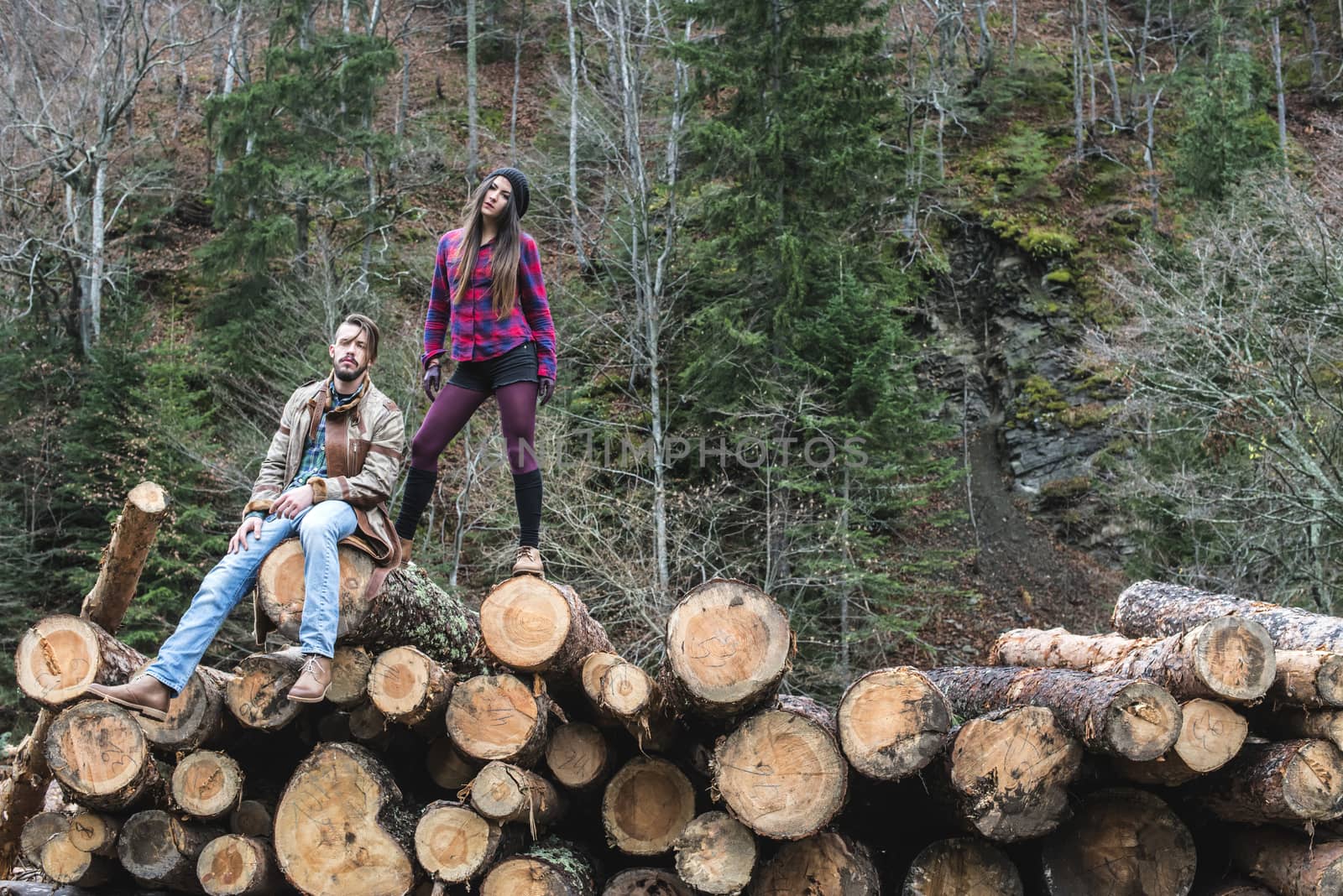 Young woman and men on wood logs in the forest