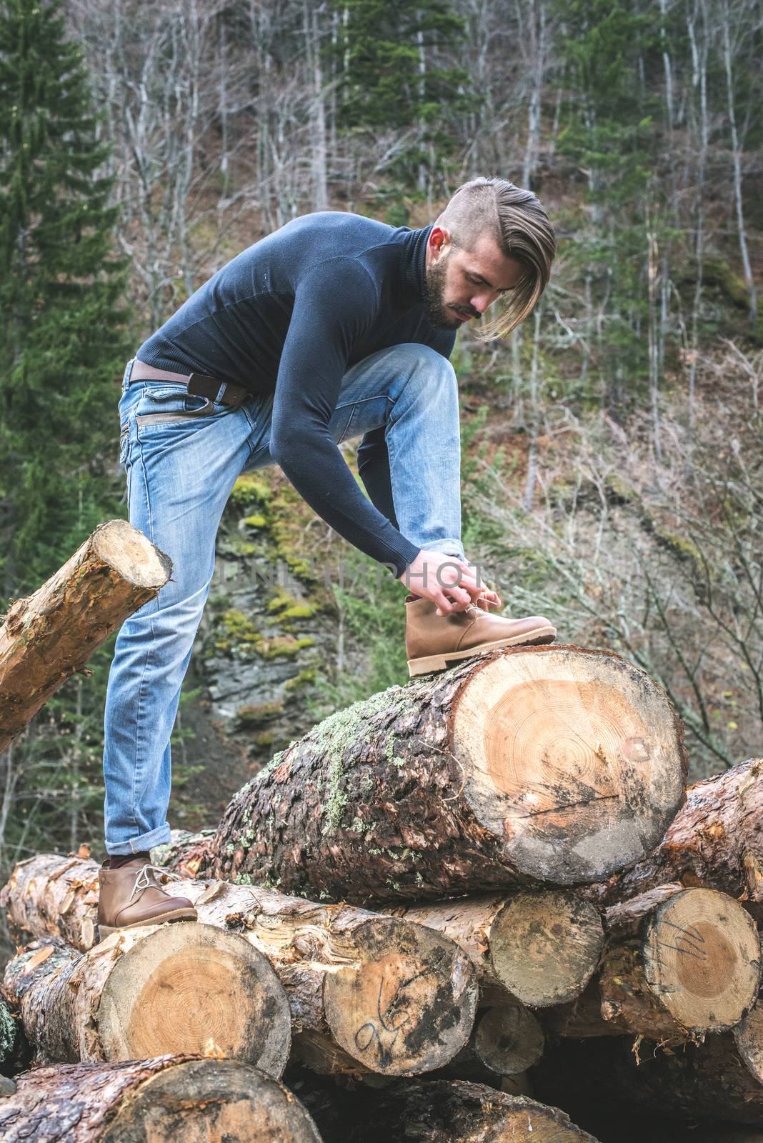 Man tie shoes on logs in the forest