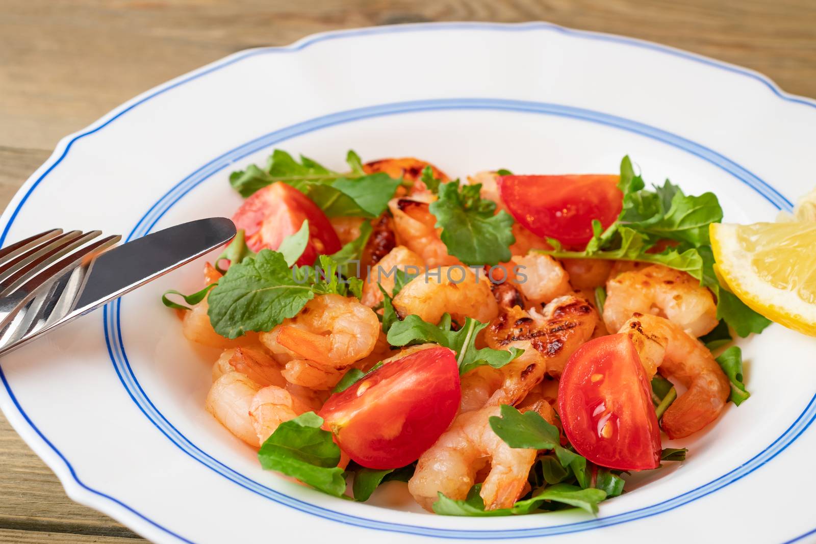 Fresh homemade salad of shrimp, arugula and tomato in a white plate on a wooden table, close up.