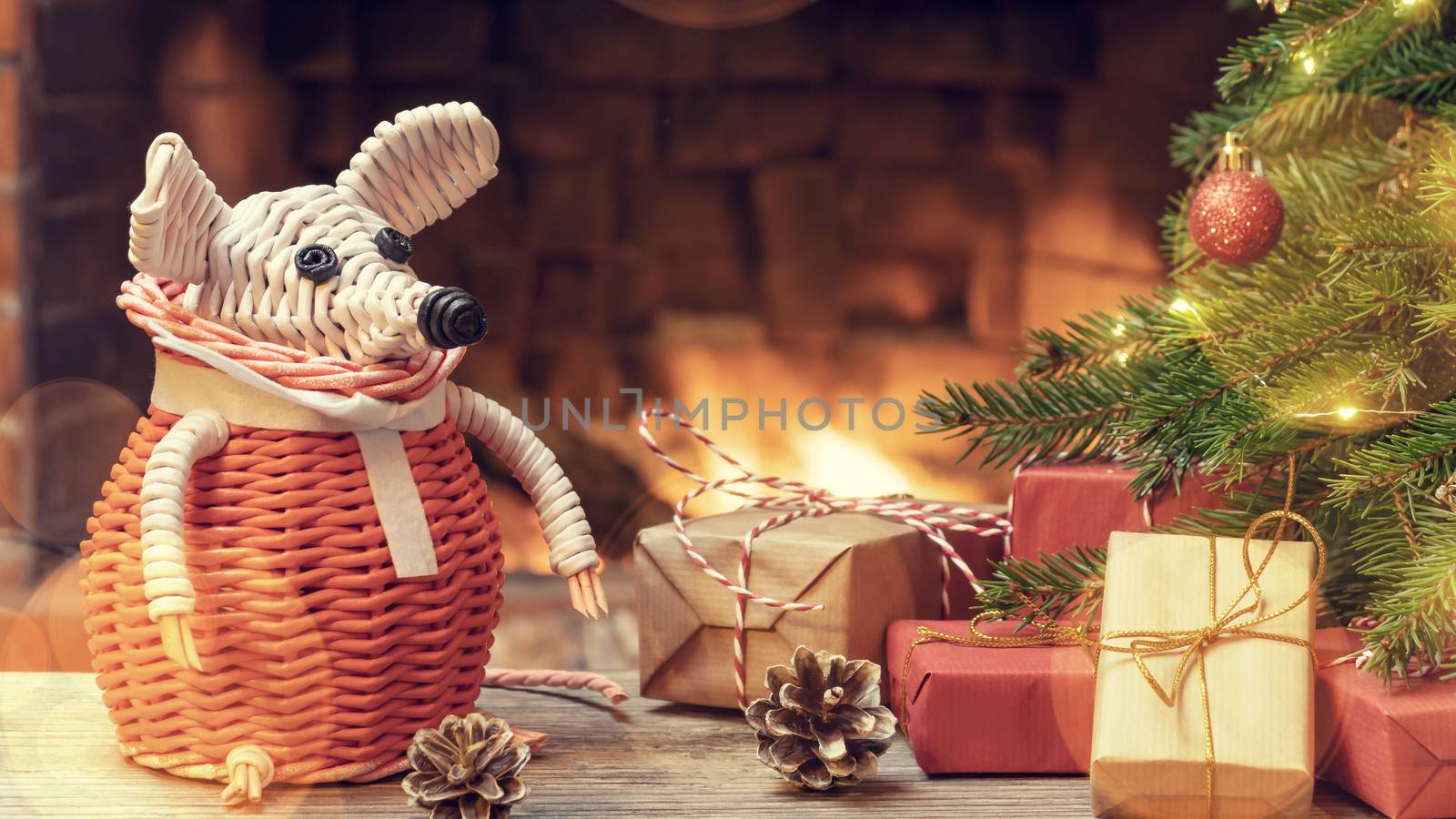 Christmas composition - a wicker white mouse - symbol of 2020 according to Chinese horoscope next to gifts under Christmas tree in room by fireplace. by galsand