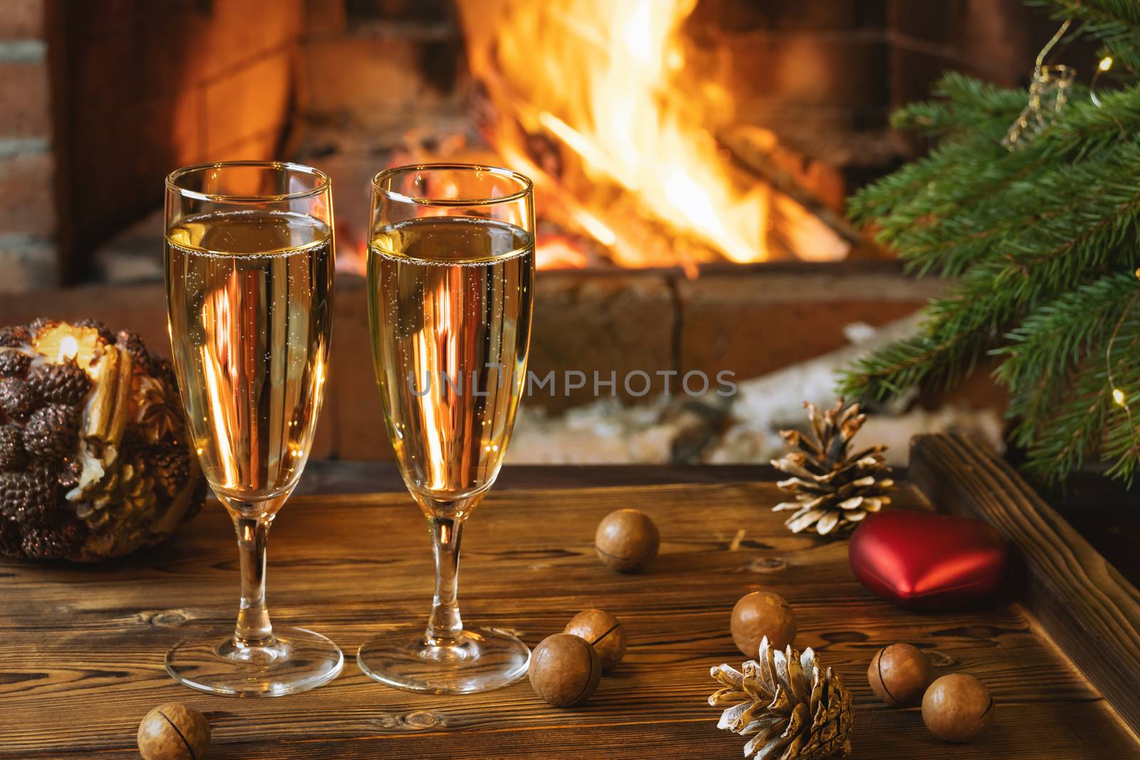 Christmas composition - Two glasses with champagne on a wooden table near a Christmas tree in a room with a burning fireplace.