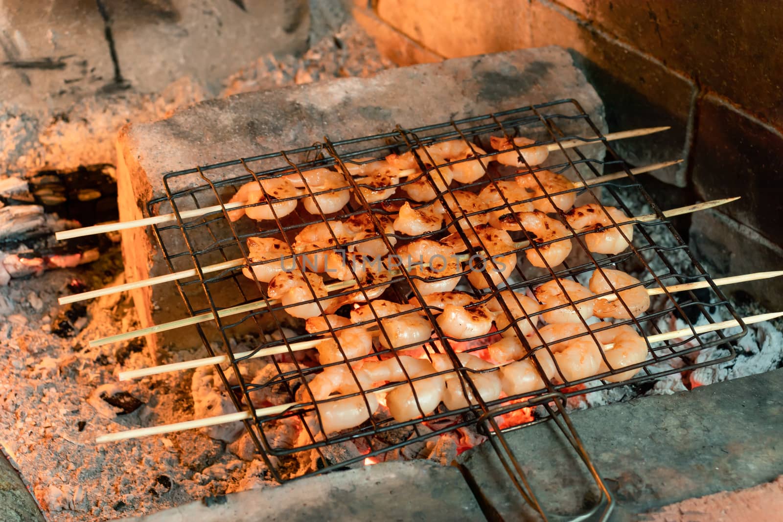 Shrimp frying on bamboo skewers on hot coals in a fireplace by galsand