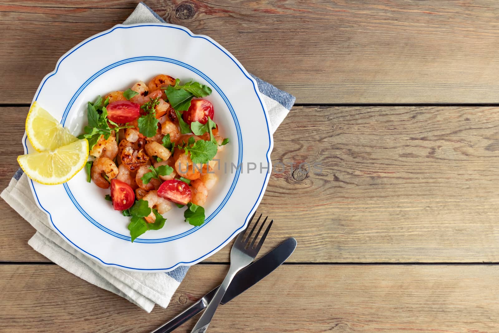 Fresh homemade salad of shrimp, arugula and tomato in a white plate on a wooden table, top view, flat lay, copyspace by galsand