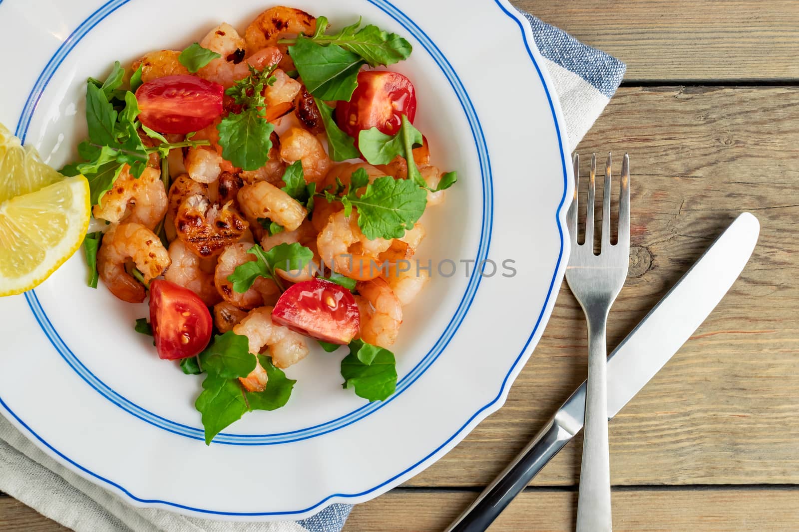 Fresh homemade salad of shrimp, arugula and tomato in a white plate on a wooden table, top view, flat lay, close up by galsand