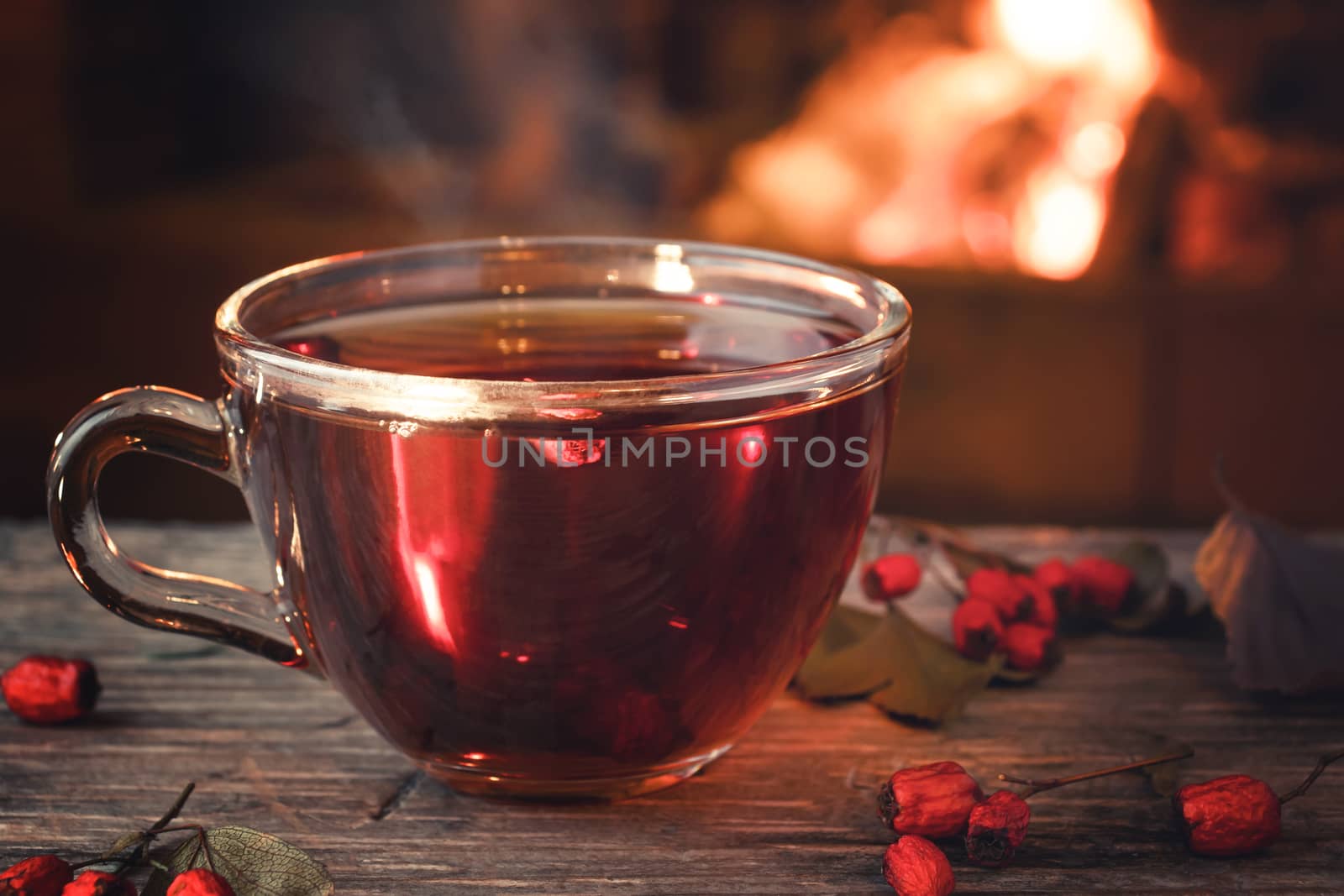 Tea with hawthorn in a glass cup on a wooden table in a room with a burning fireplace.