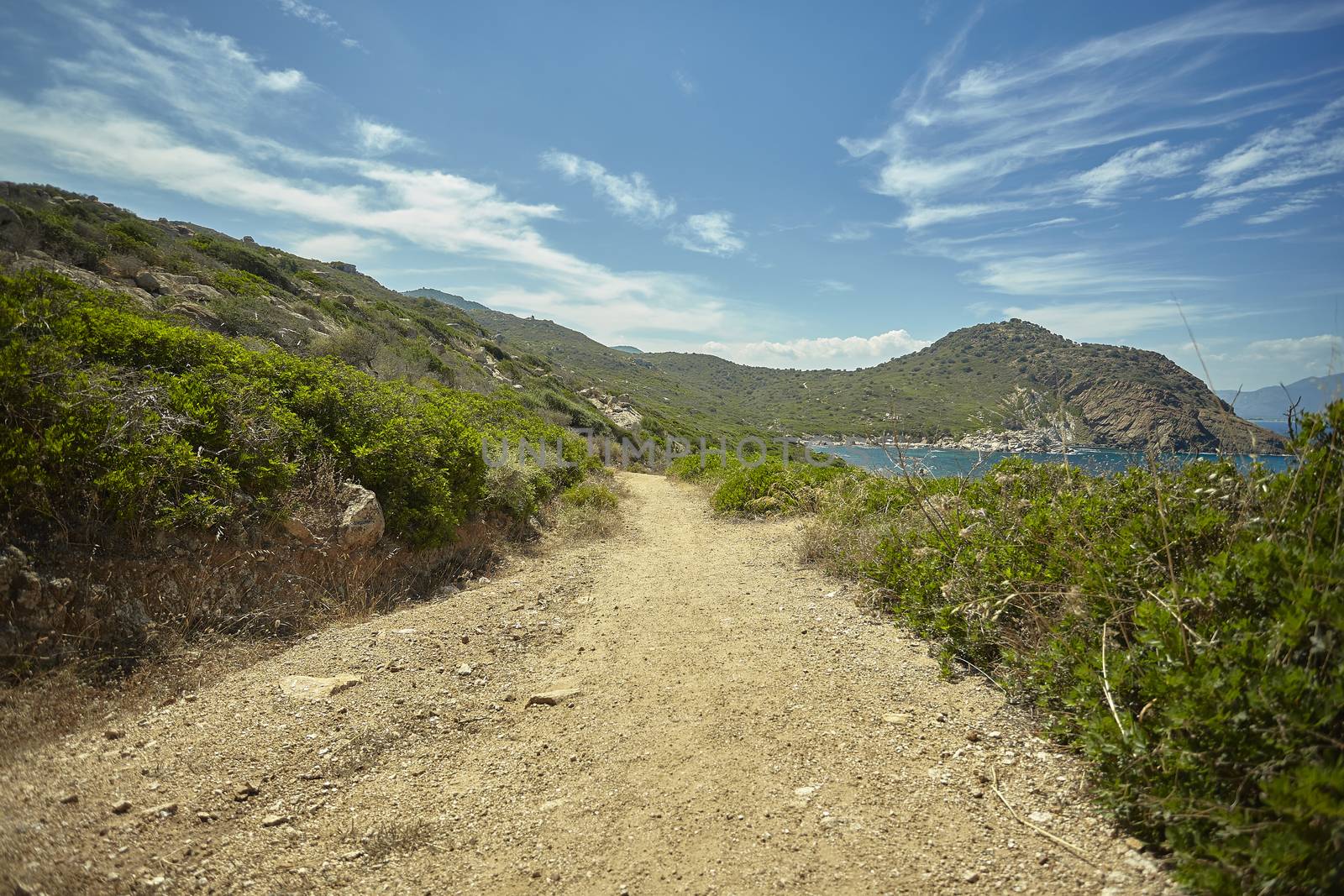 Small dirt path that runs along the coast of an area of southern Sardinia with a precipice on the side of the sea.