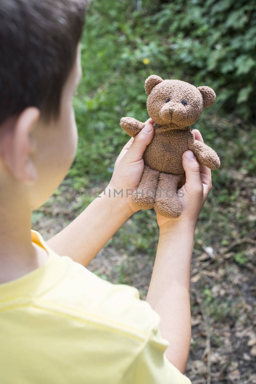 Child hold teddy in a garden. 