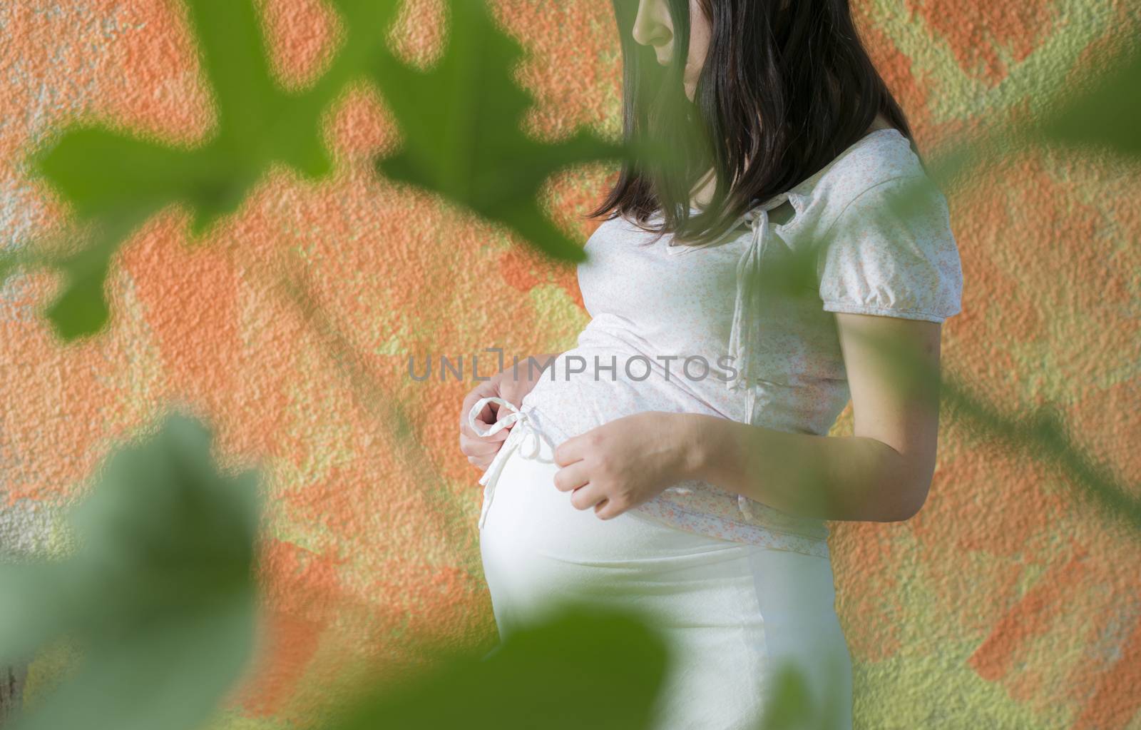 Pregnant women in front of orange wall. White dress