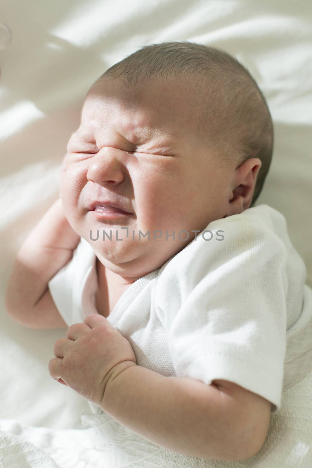 Unhappy frowning baby. White clothes