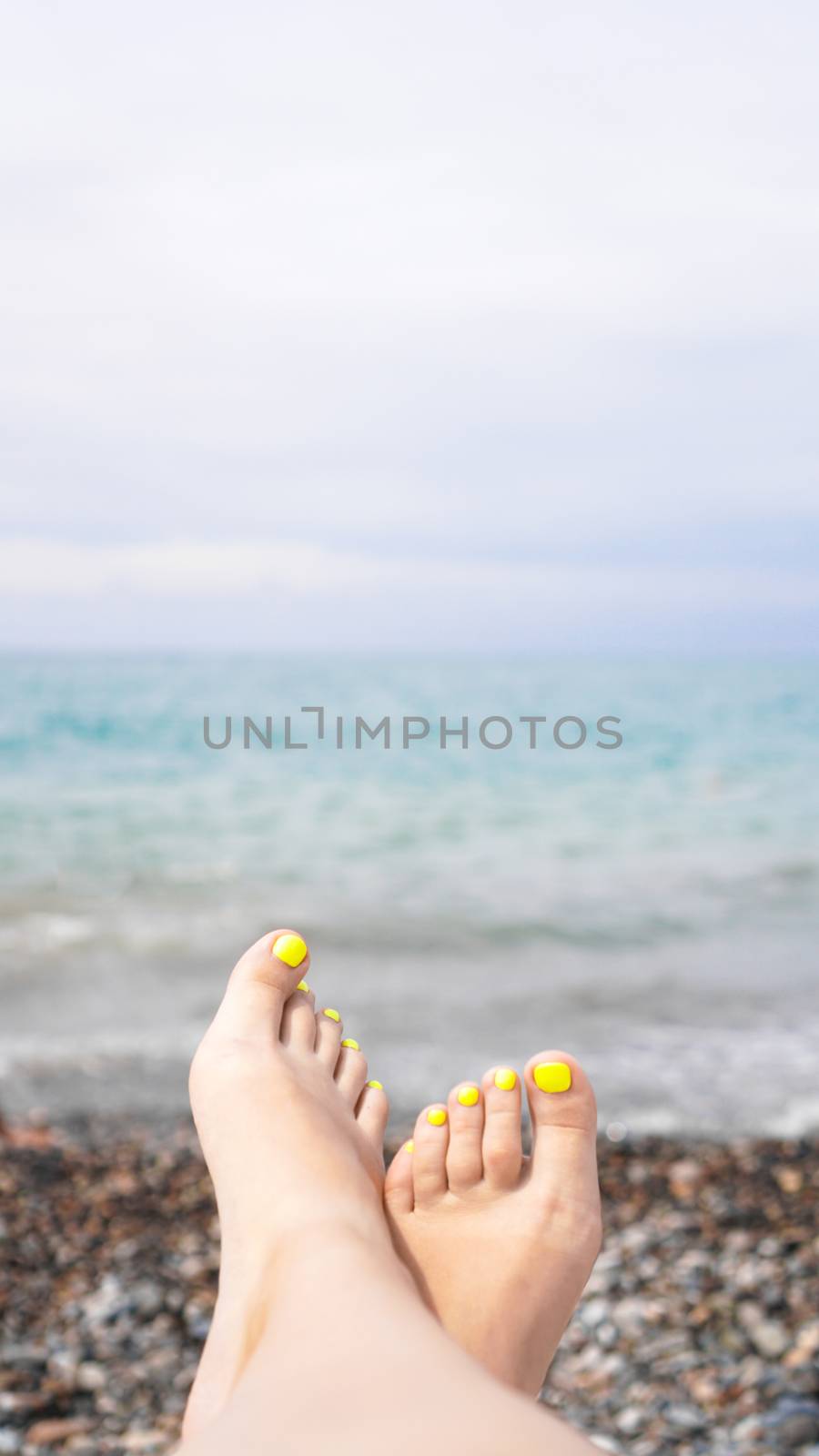 Woman lying near water. Woman legs near blue sea - vertical photo