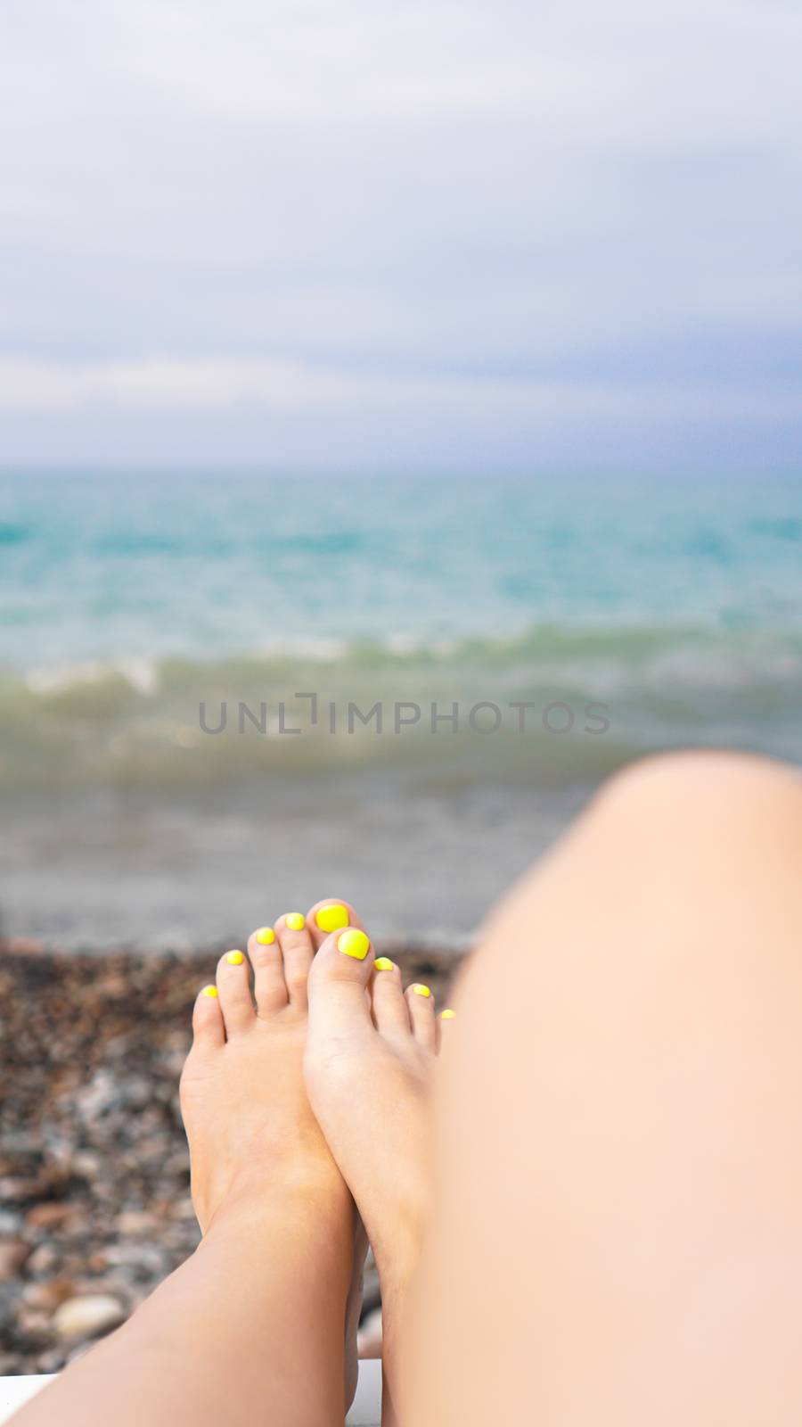Woman lying near water. Woman legs near blue sea - vertical photo