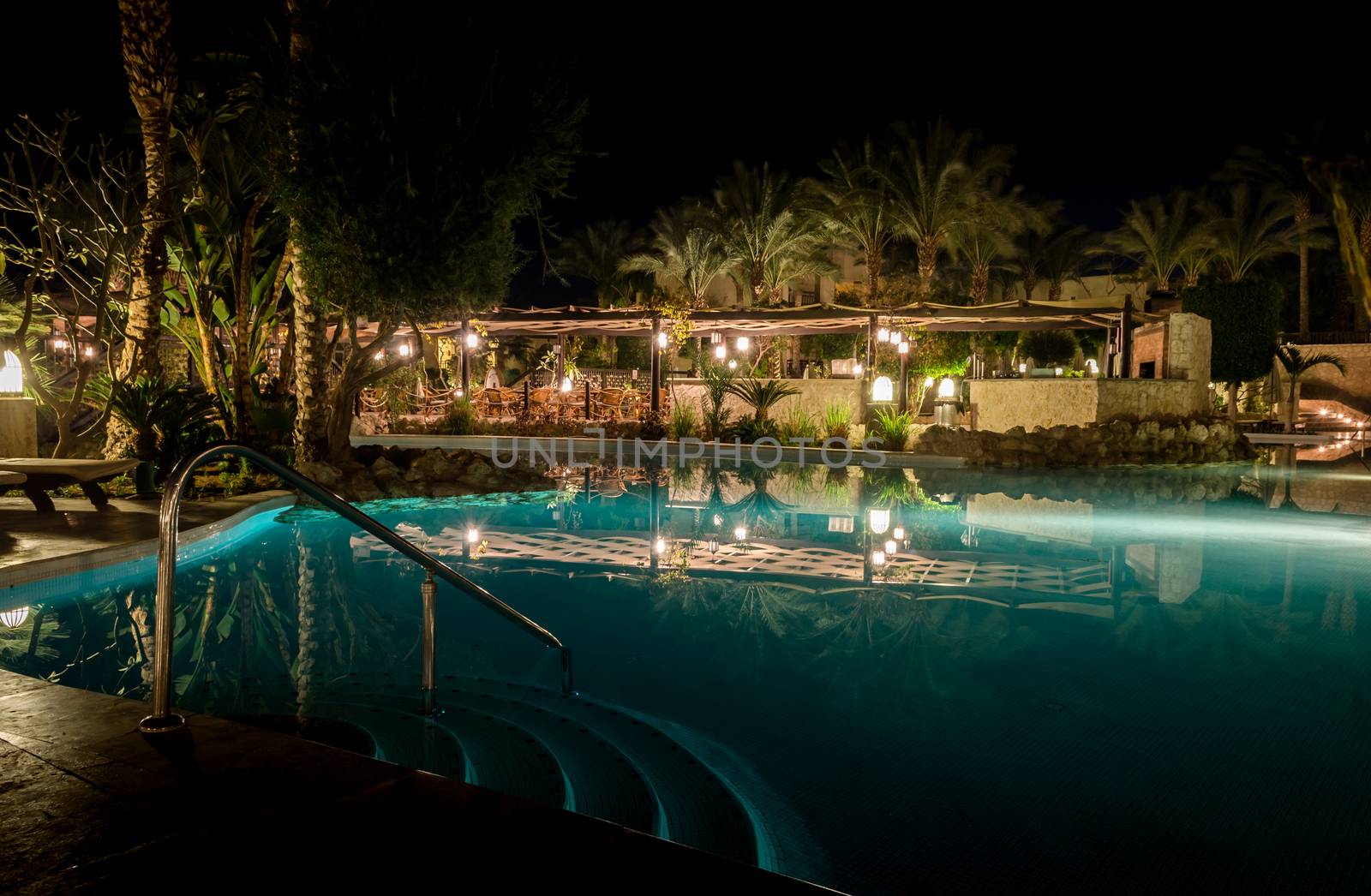 Sharm El Sheikh, Egypt - 02 06 2018: night in the hotel aquamarine pool empty armchairs in the bar palm trees light lanterns reflected in the water