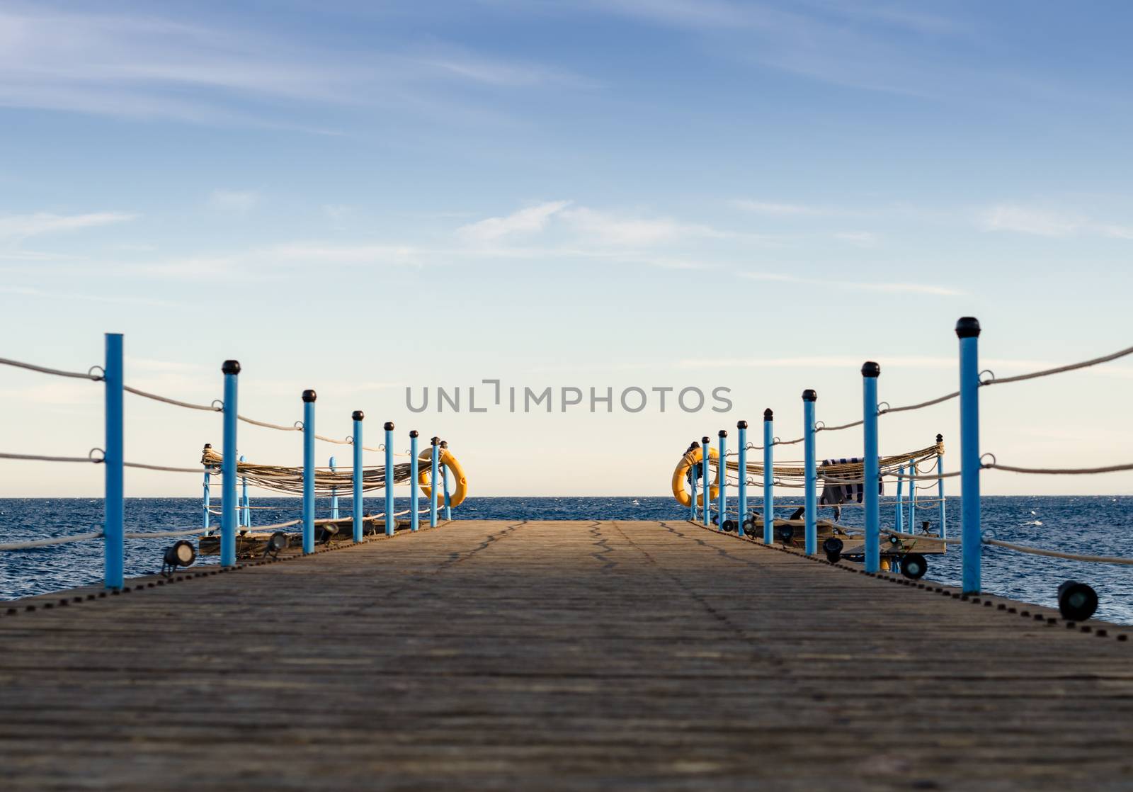 wooden platform with blue posts with ropes and orange lifebuoys on the background of the sea and sky with clouds