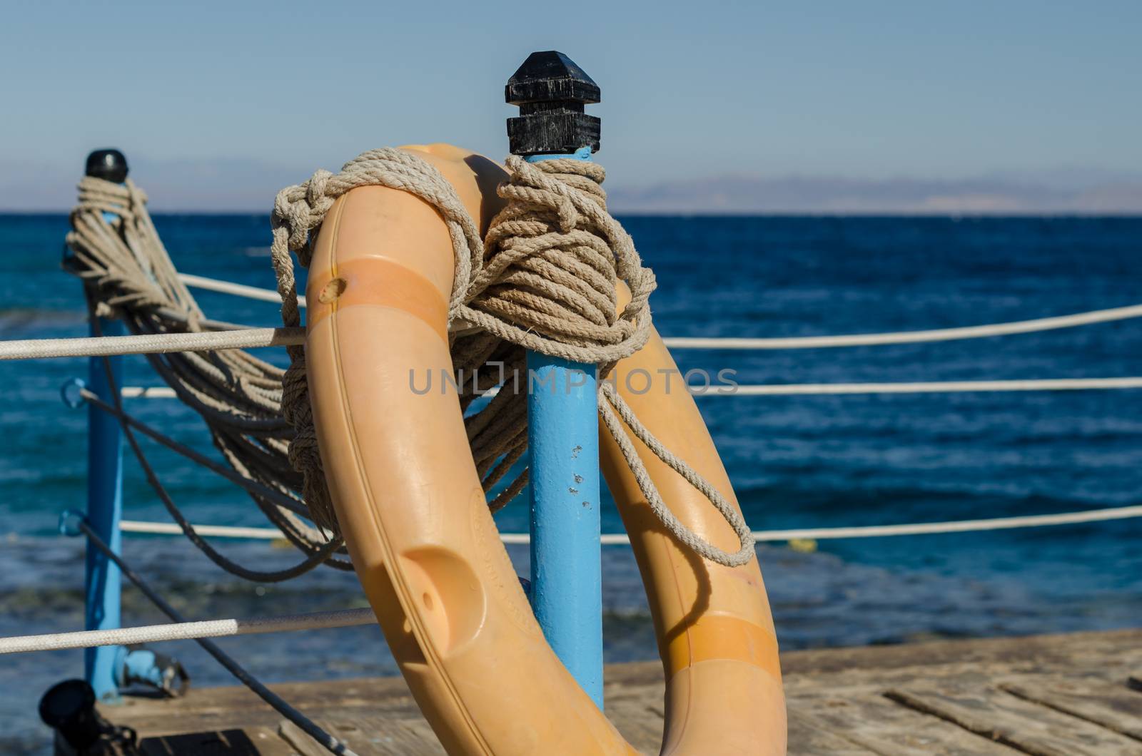 orange lifebuoy on a wooden table with ropes on a wooden platform on a background of blue sea close up