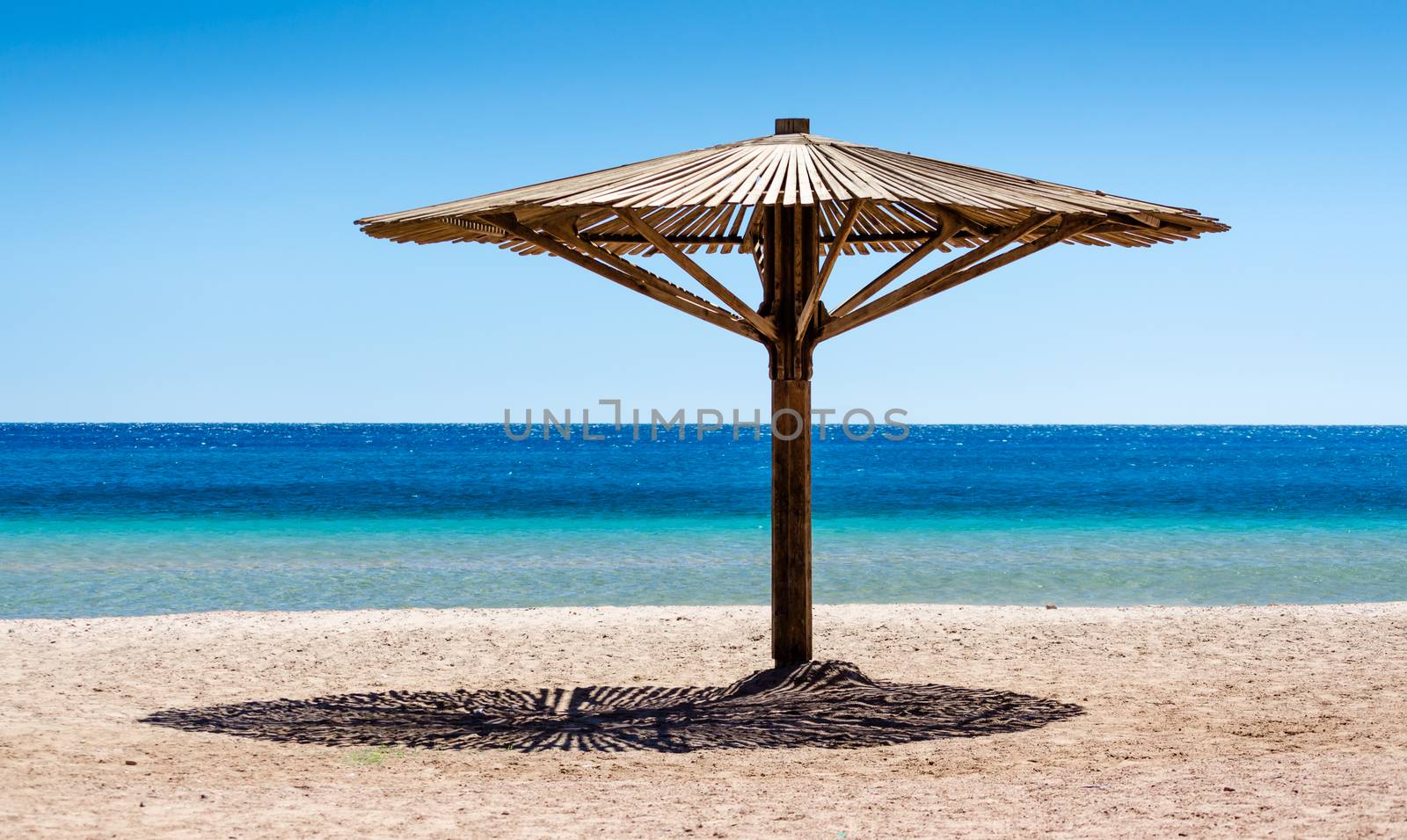 one wooden beach umbrella on the sand on the beach against the blue water of the Red Sea