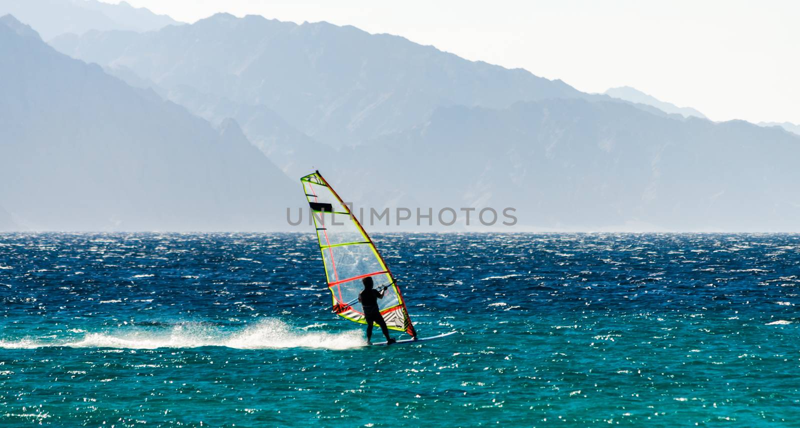 one surfer rides a sail in the Red Sea against the backdrop of the high mountains in Egypt