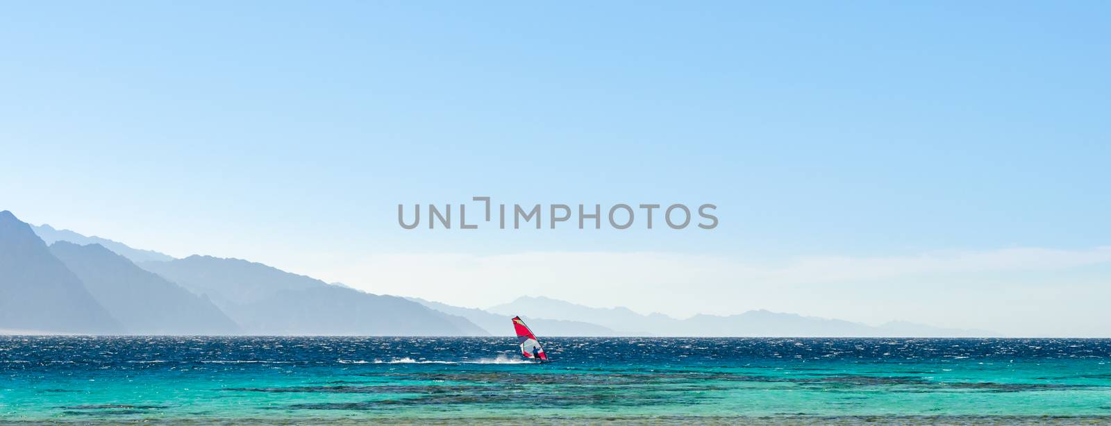 surfer rides in the Red Sea against the backdrop of high rocky mountains and a blue sky with clouds in Egypt Dahab
