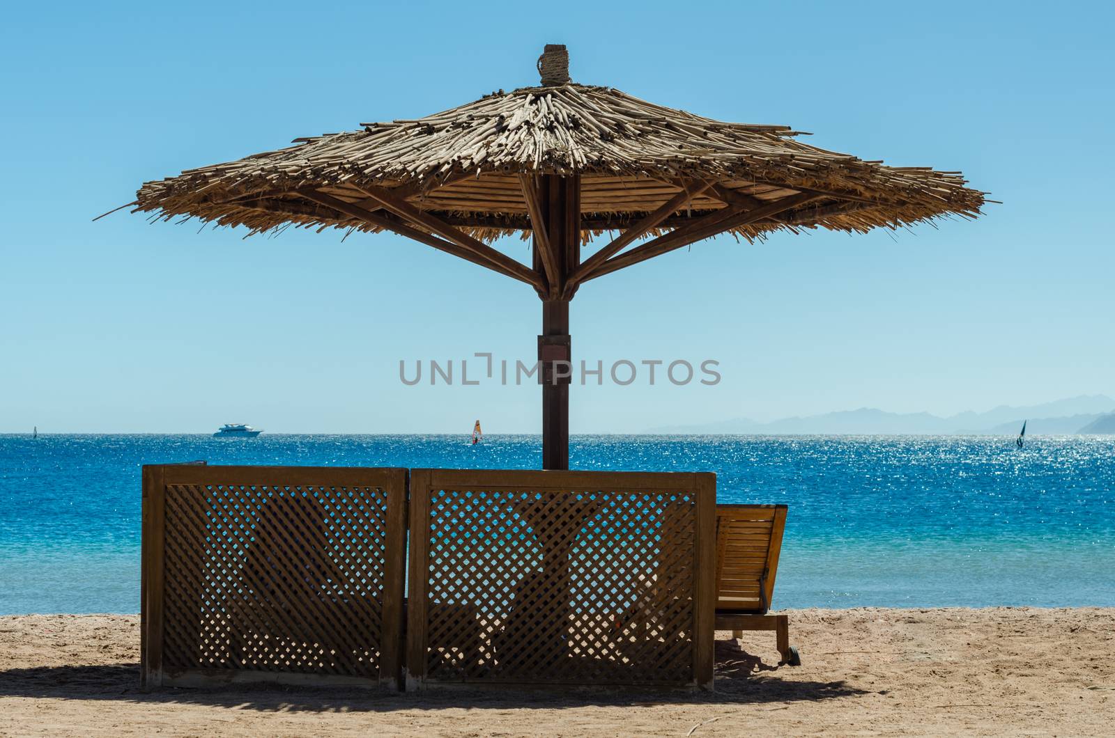 wooden loungers under a bamboo beach umbrella on the beach against the sea and blue sky