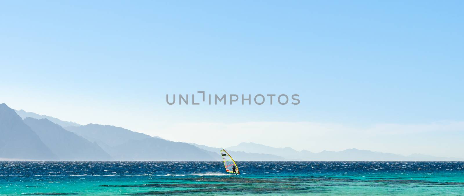 surfer rides in the Red Sea against the backdrop of high rocky mountains and a blue sky with clouds in Egypt Dahab