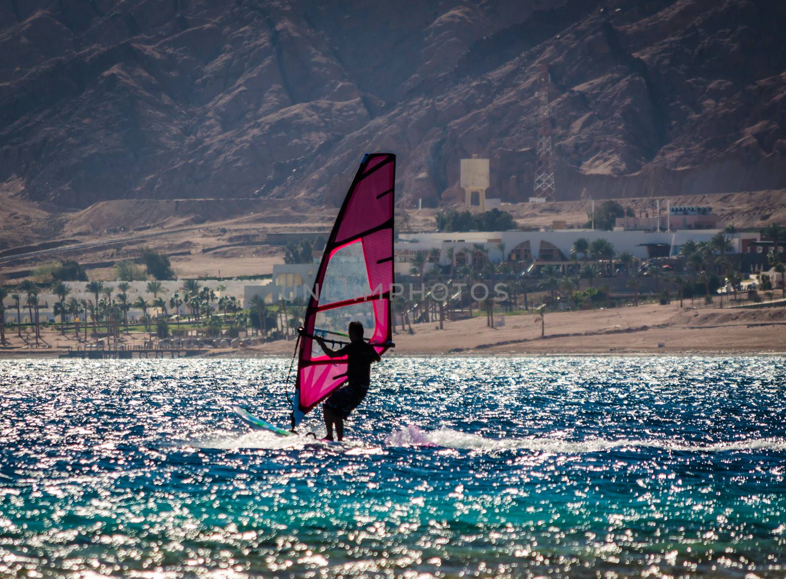 silhouette of a surfer in the Red Sea on the background of a rocky coast with palm trees and a hotel in Egypt