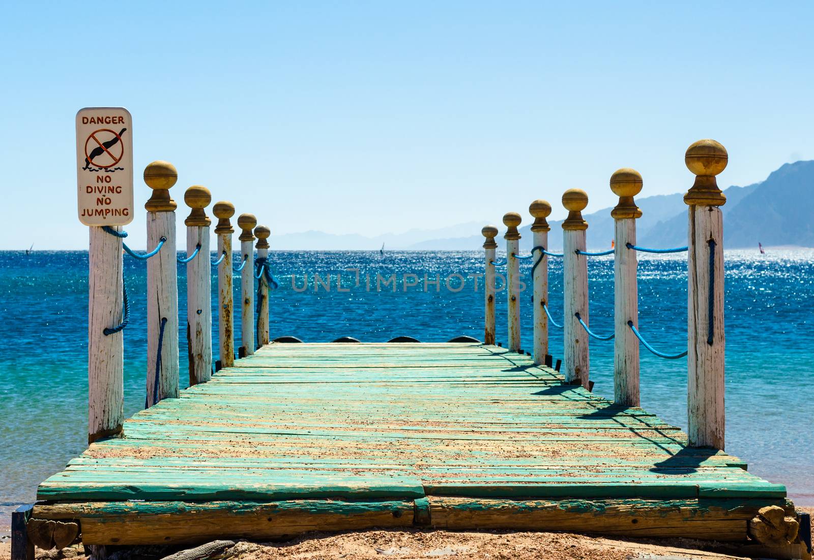 wooden pier with columns and a warning sign against a blue sea and mountains on the horizon