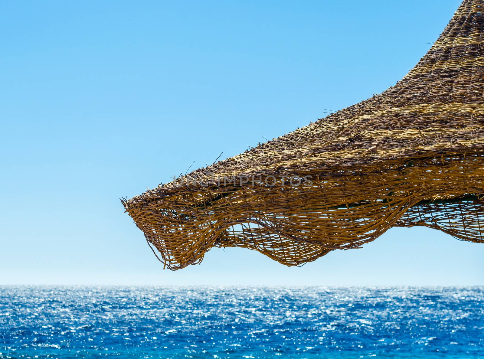 fragment of a wicker beach umbrella against the backdrop of the sea and a clear blue sky