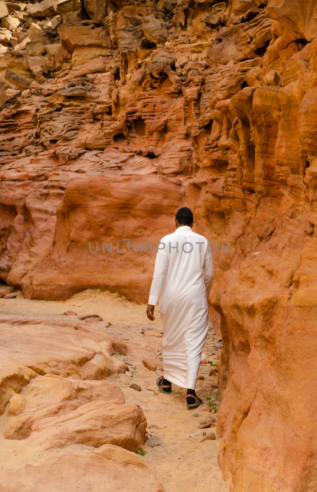 man in white arab clothing walks in a colored canyon