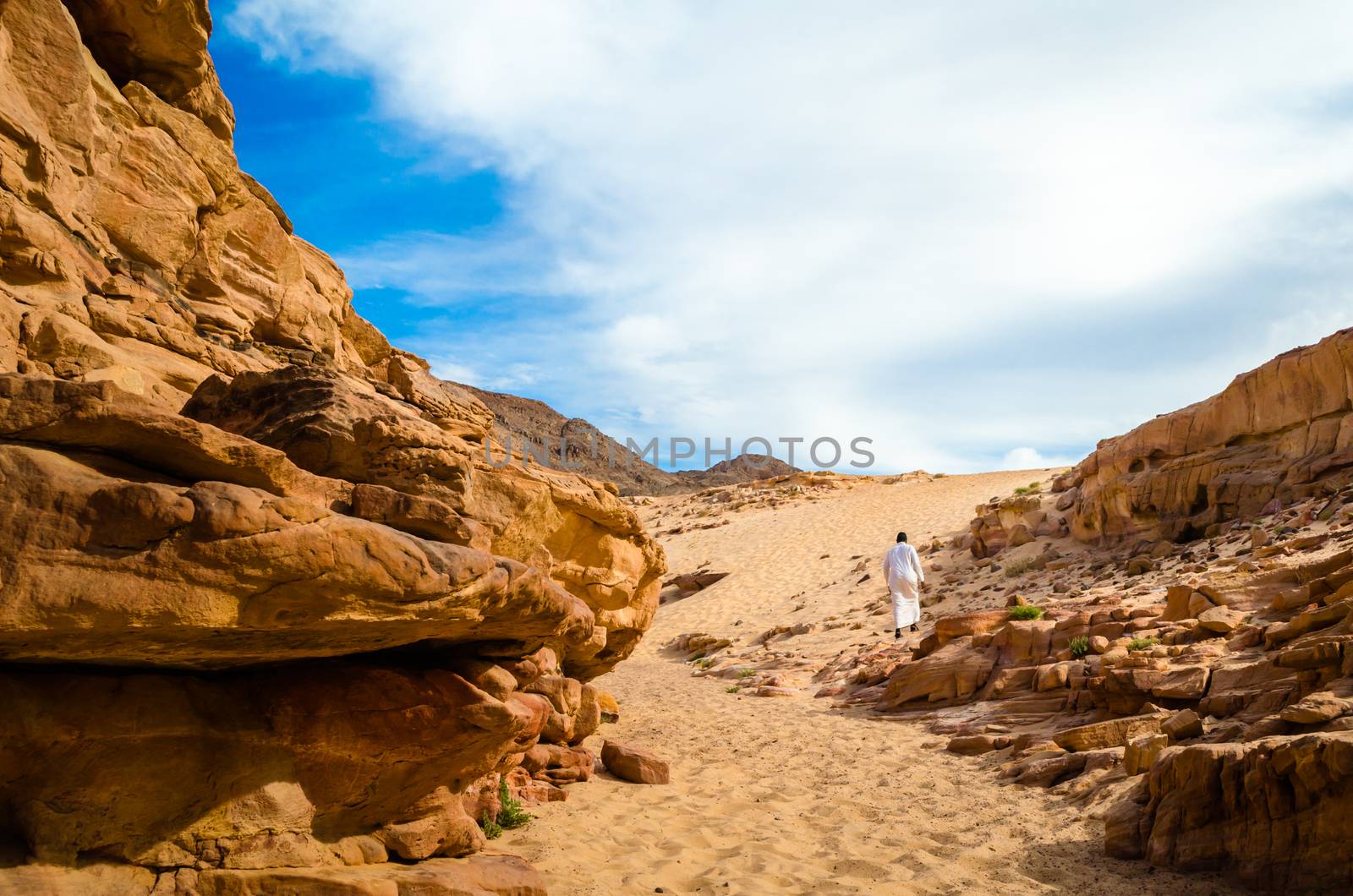 man in white arab clothing walks in a colored canyon in Egypt Dahab