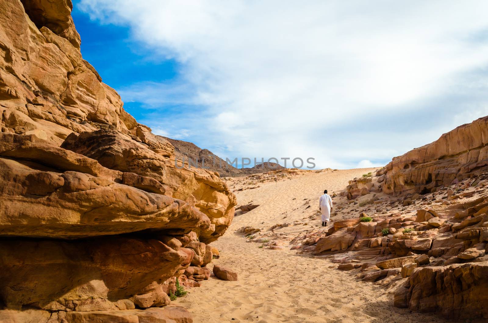 man in white arab clothing walks in a colored canyon in Egypt Dahab
