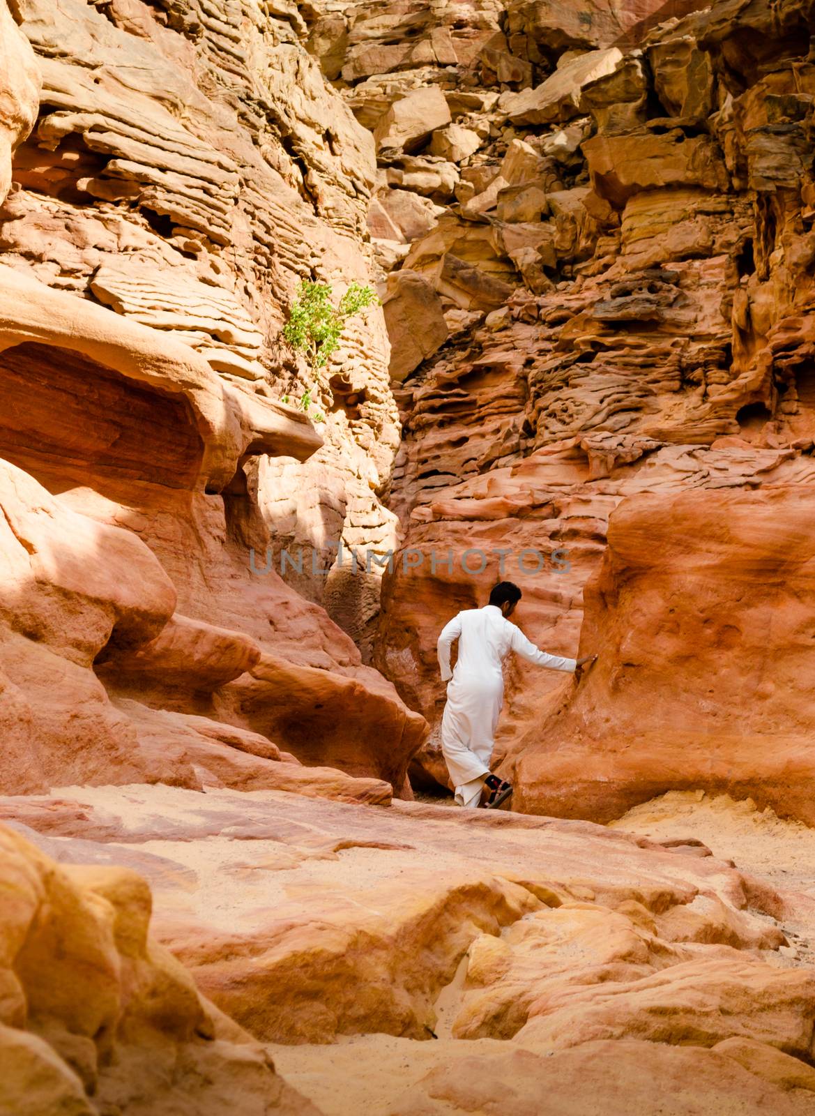 man in white arab clothing walks in a colored canyon