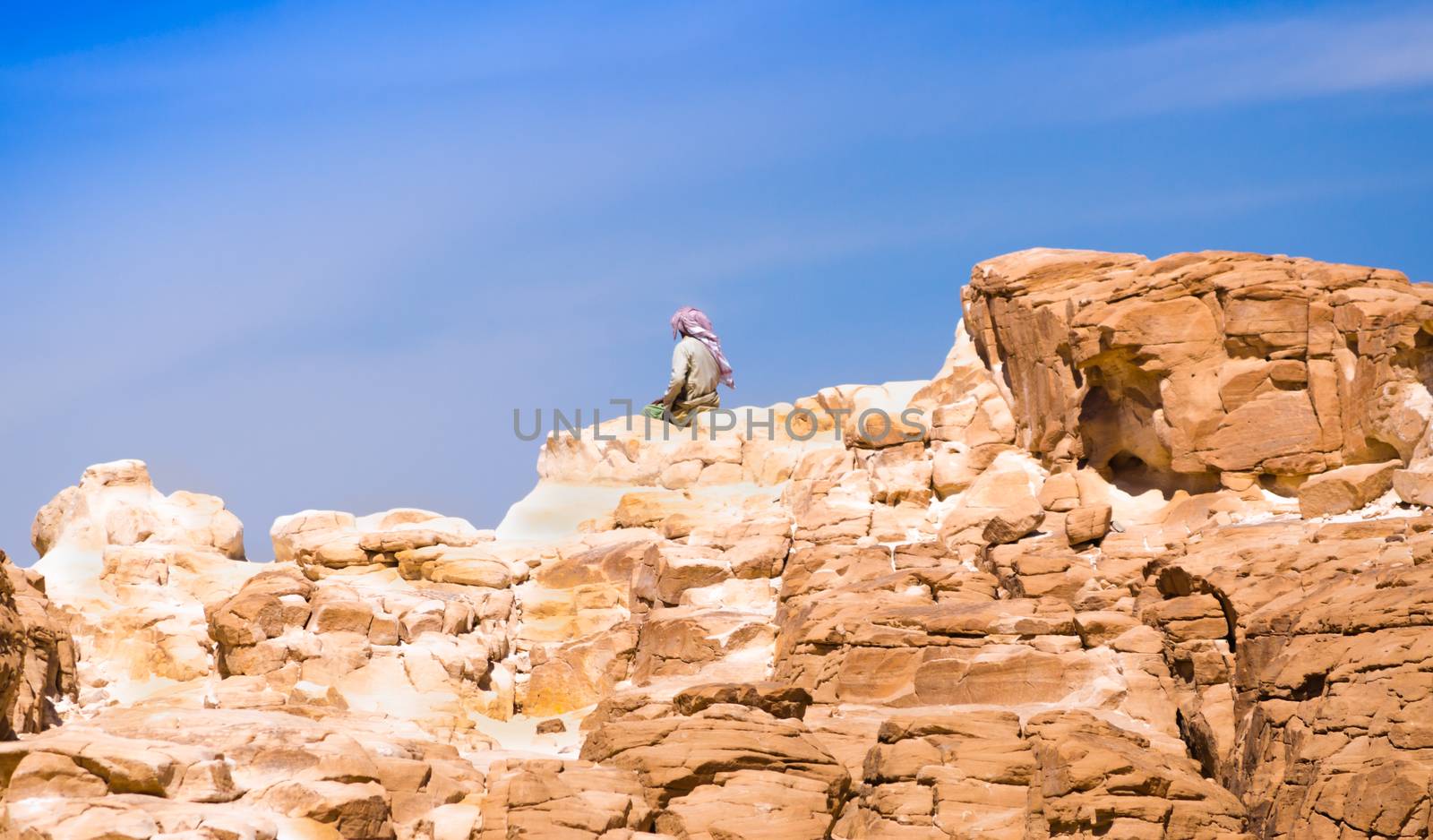 Bedouin sitting on the peak of a high stone rock against a blue sky in Egypt Dahab