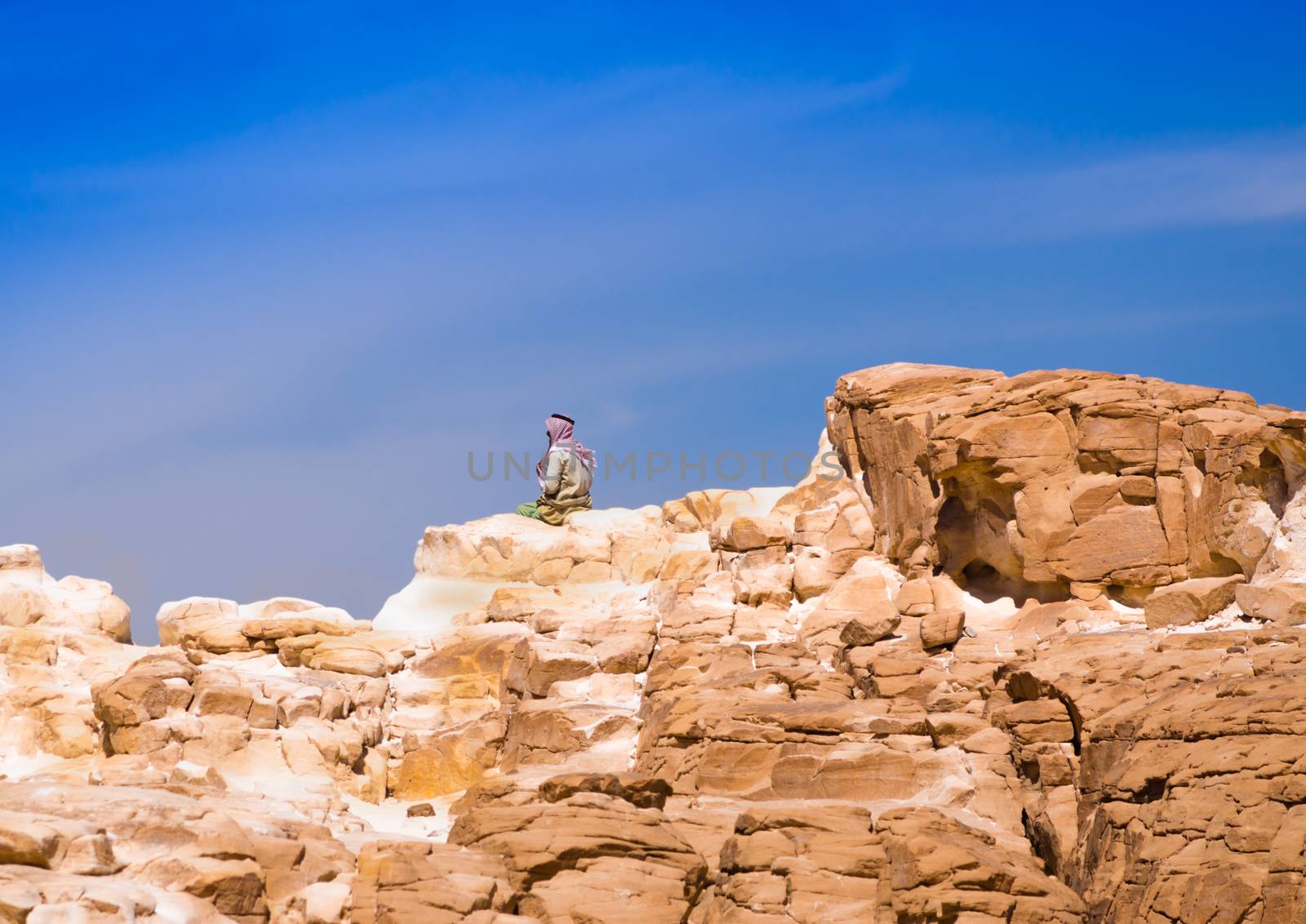 Bedouin sitting on the peak of a high stone rock against a blue sky in Egypt Dahab