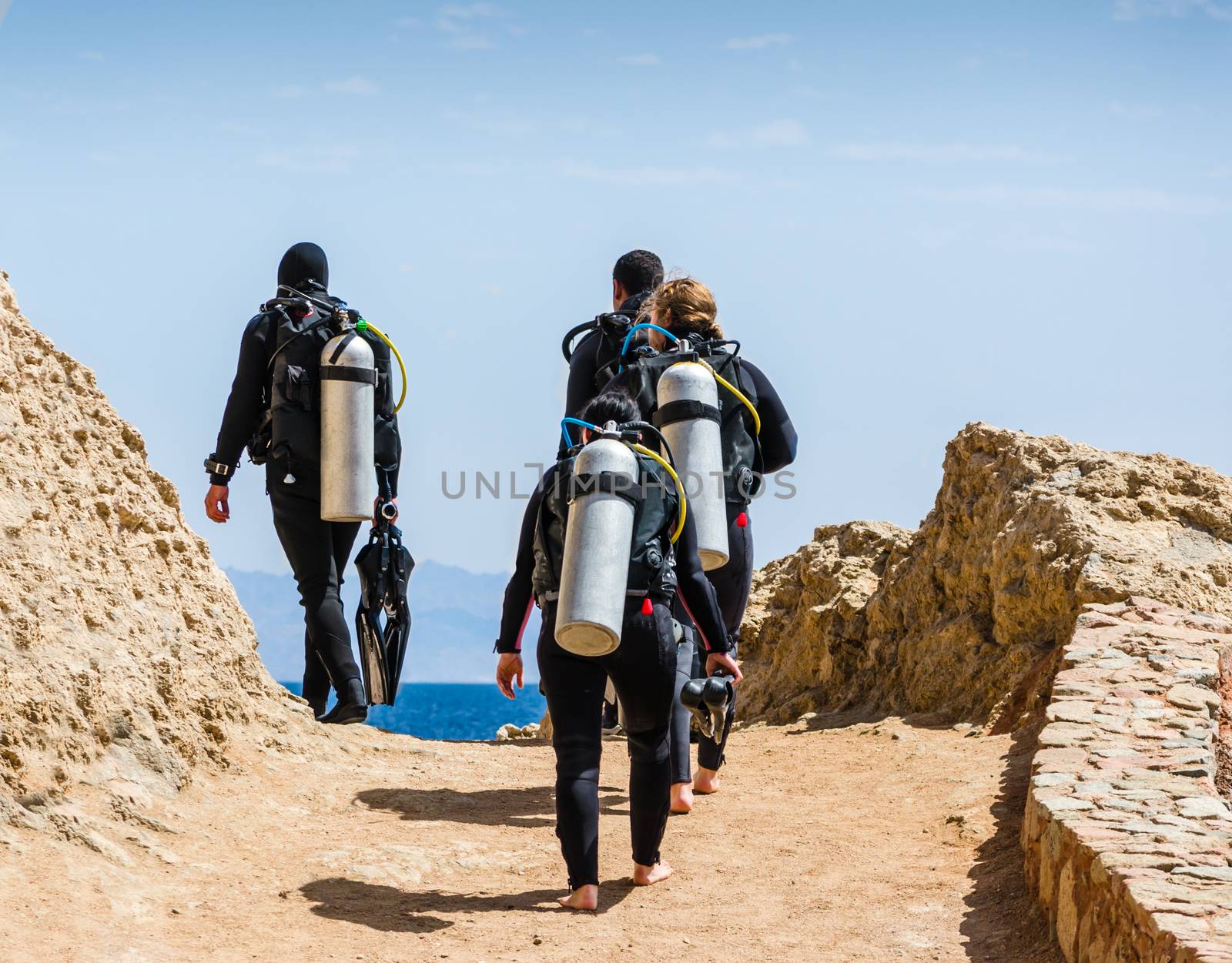 group of divers with equipment for diving go to the sea against the blue sky and clouds in Egypt Dahab