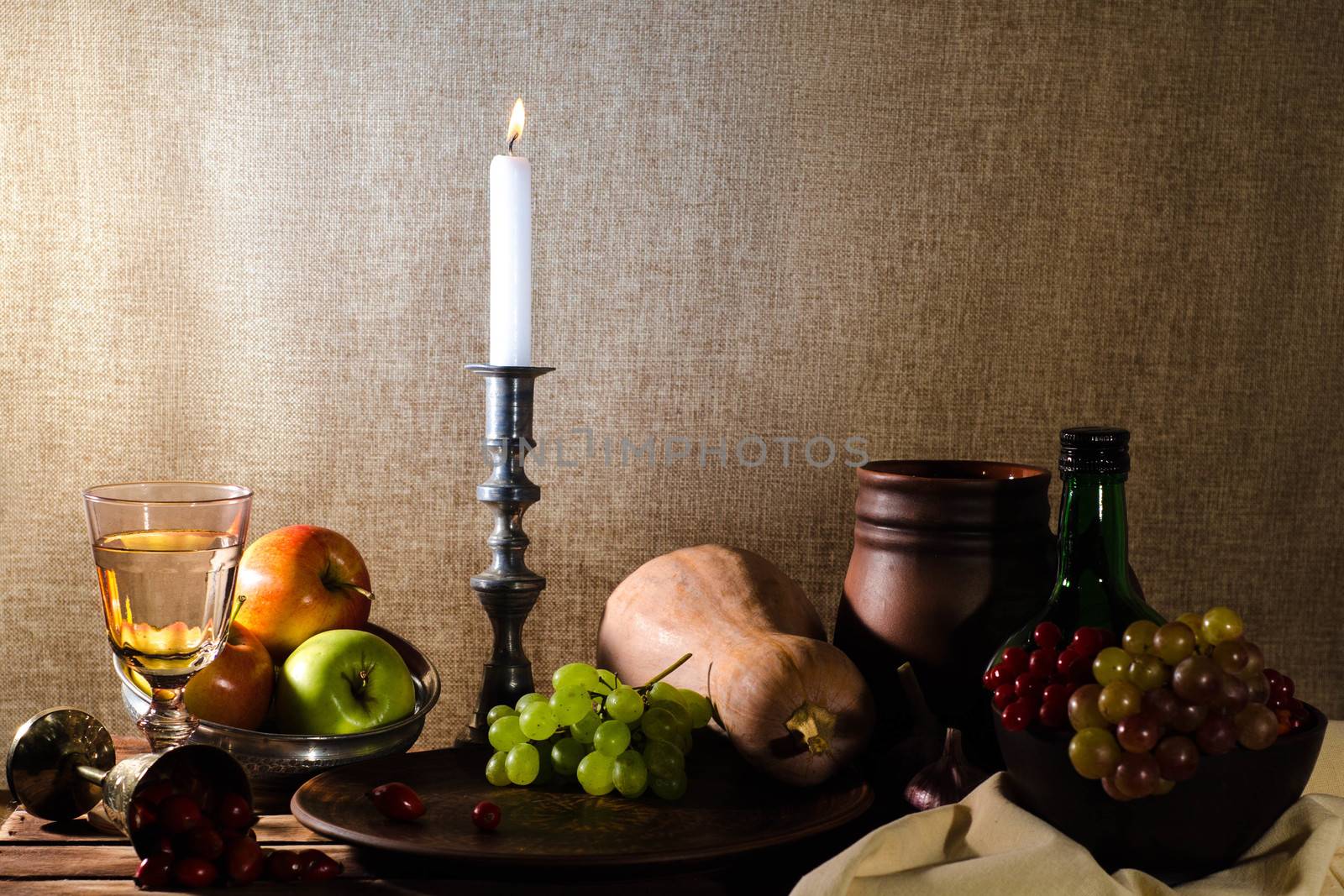 rustic still life with pumpkin grapes dog rose clay mug green bottle grapes viburnum apples glass and tin glasses and a burning candle in a candlestick.
