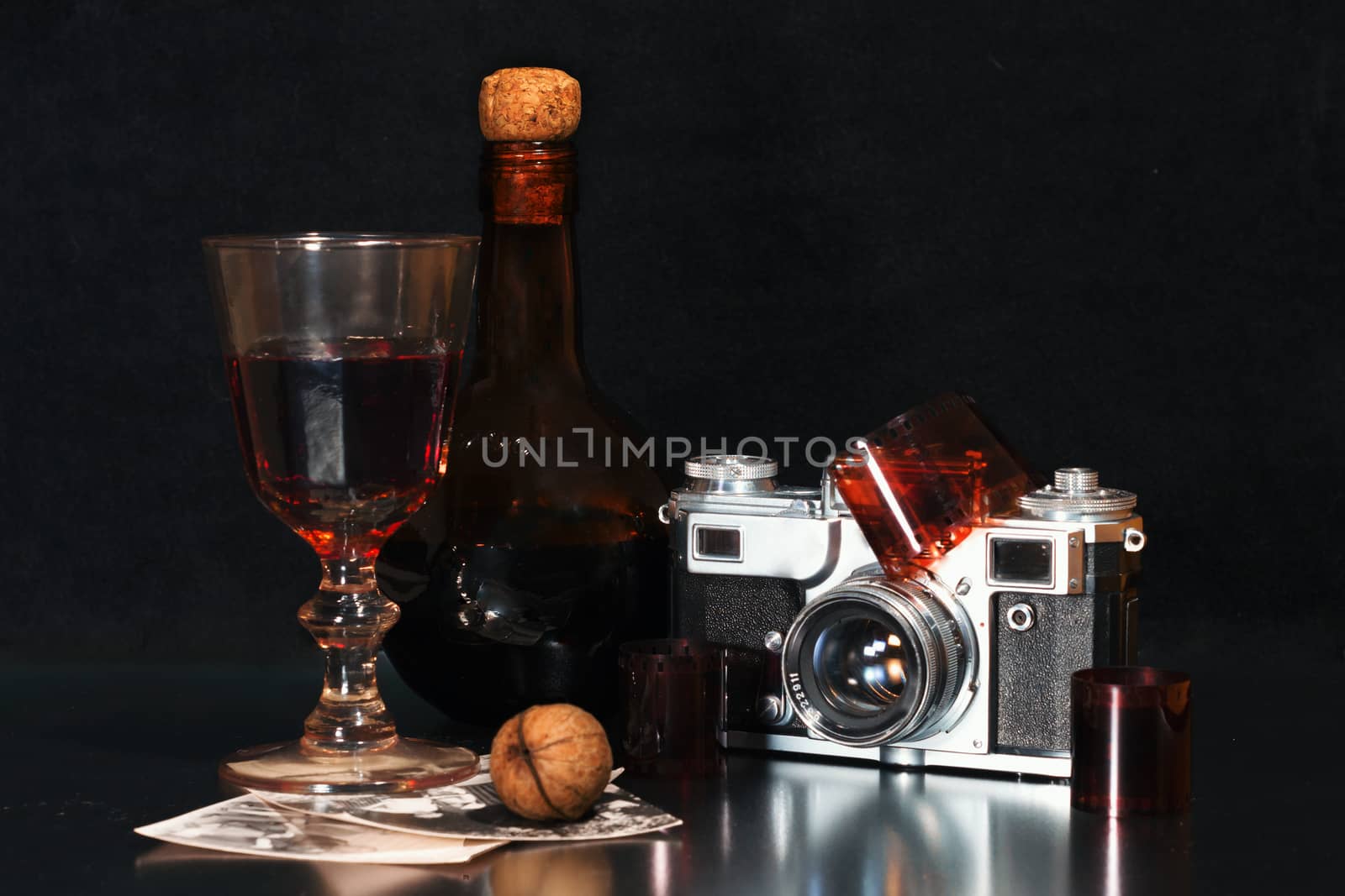 nostalgia still life with an old-fashioned camera brown bottle of alcohol rare photos and walnut