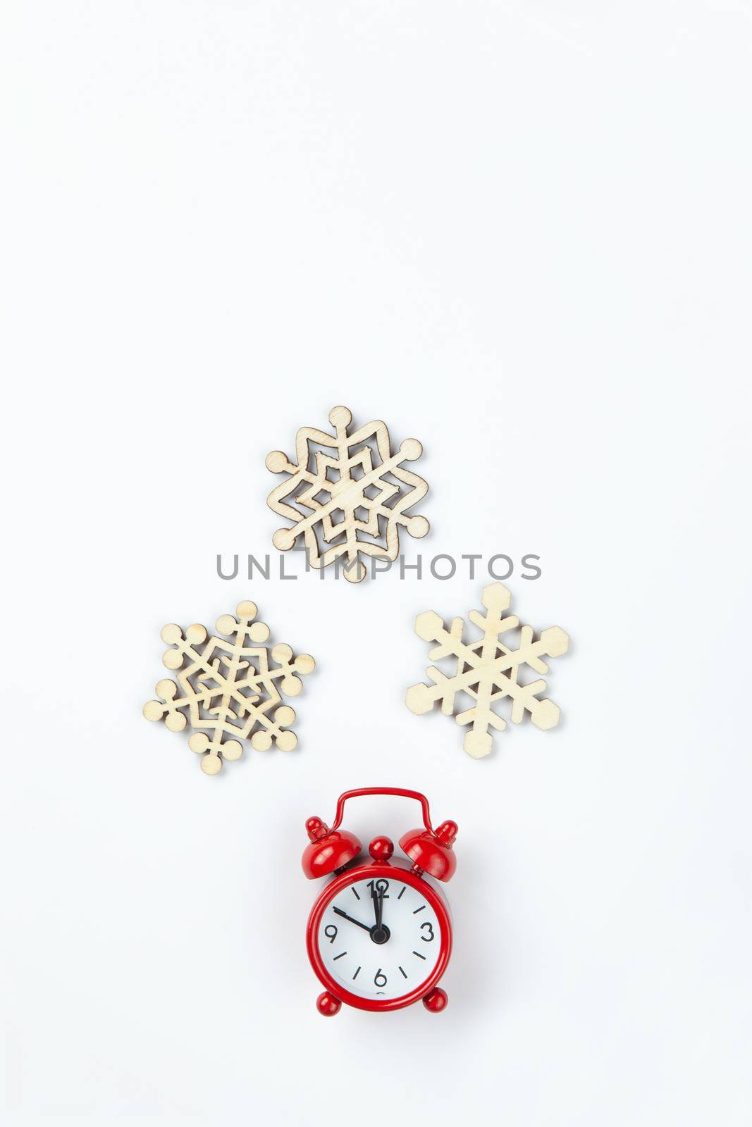 Simple Christmas composition. Small analog red clock, wooden snowflakes on white background. Minimal style flat lay, for social media. Top view. Celebration concept.